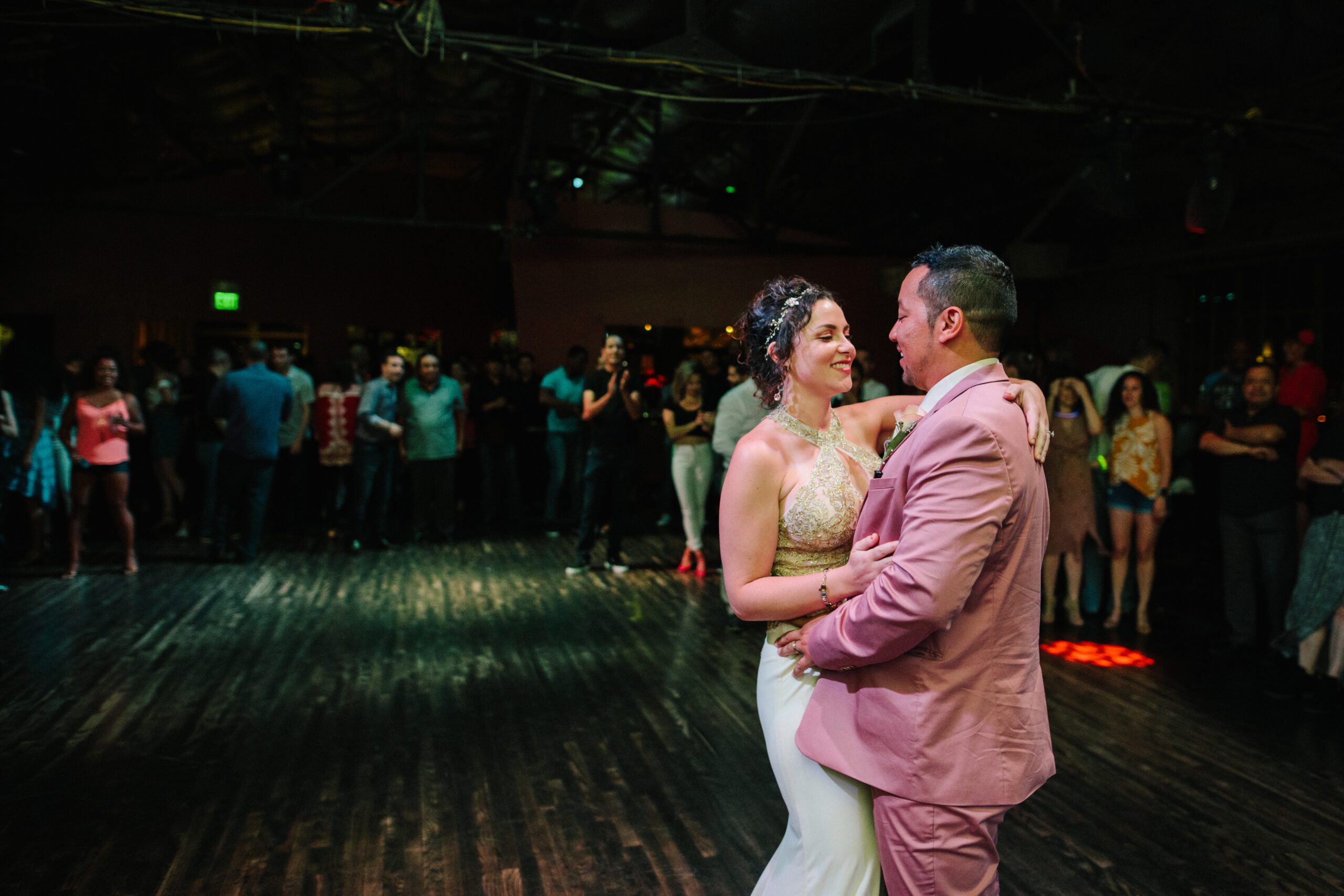 The bride and Groom dancing after their Butterfly Pavilion Wedding, the same place they met La Rumba Latin dance club. They are smiling at each other while their guests watch in awe behind them. 