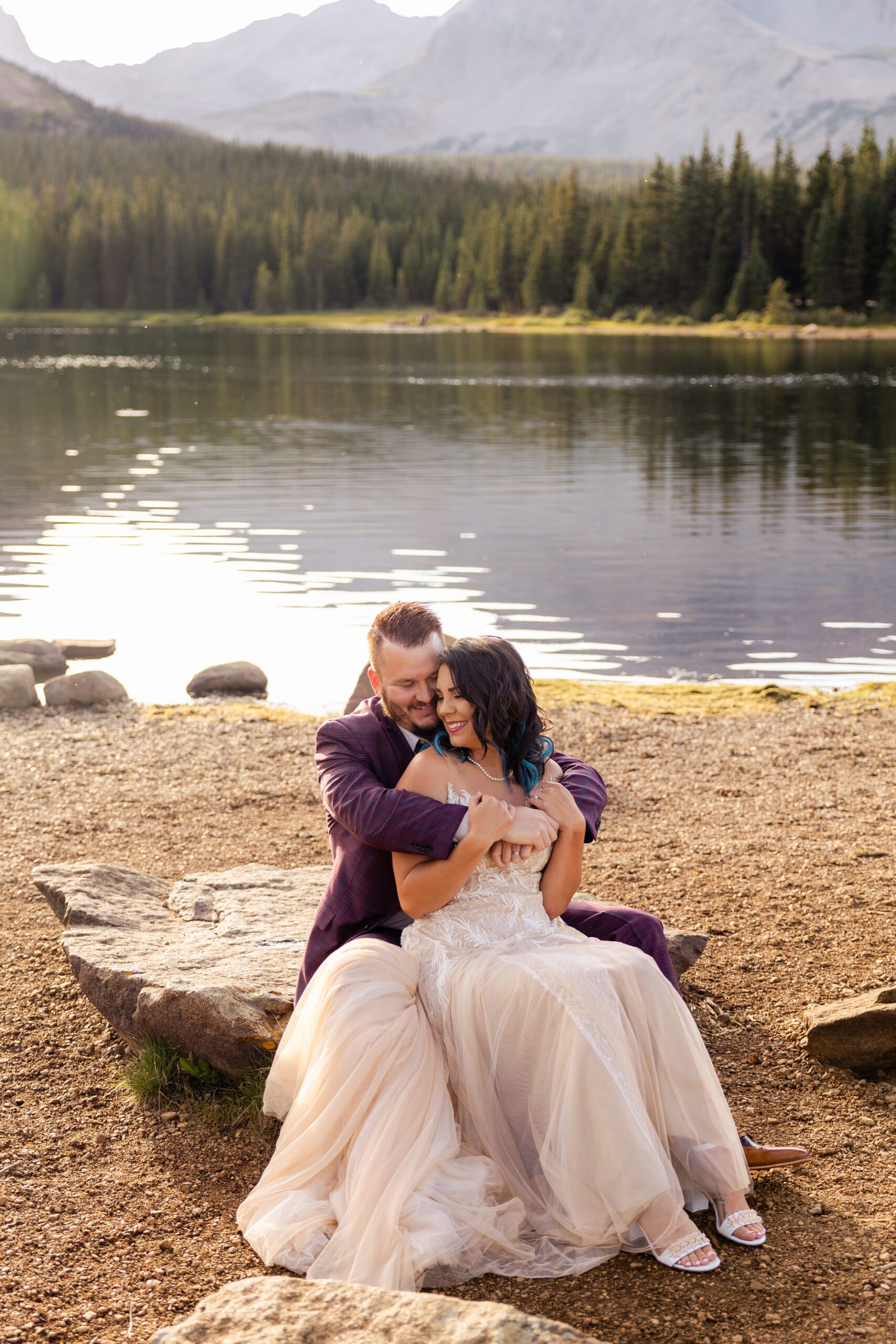 the bride and groom sitting together on a rock near the lake, wrapped up in eachothers arms after their Brainard Lake Elopement.