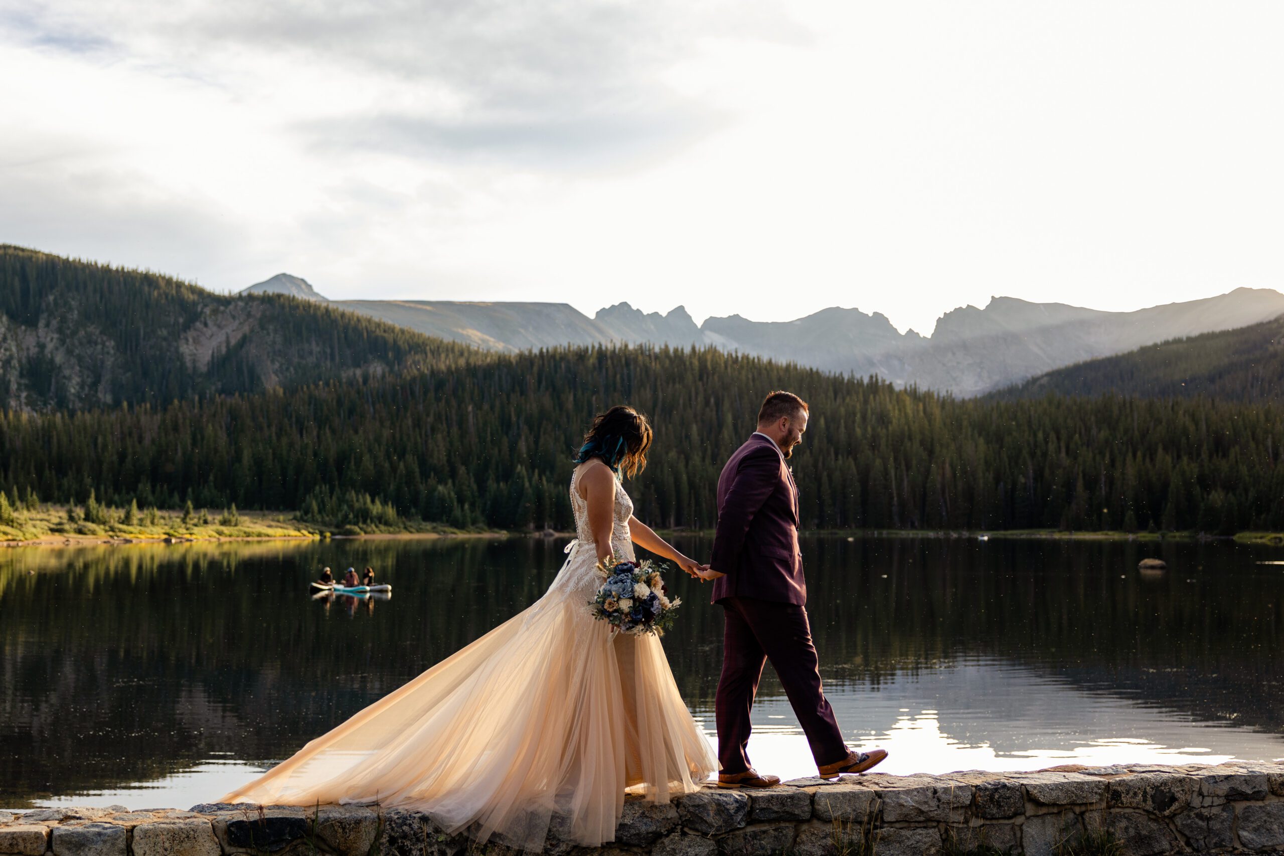 The bride and groom walk above the lake on a cozy ledge during their Brainard Lake Elopement.