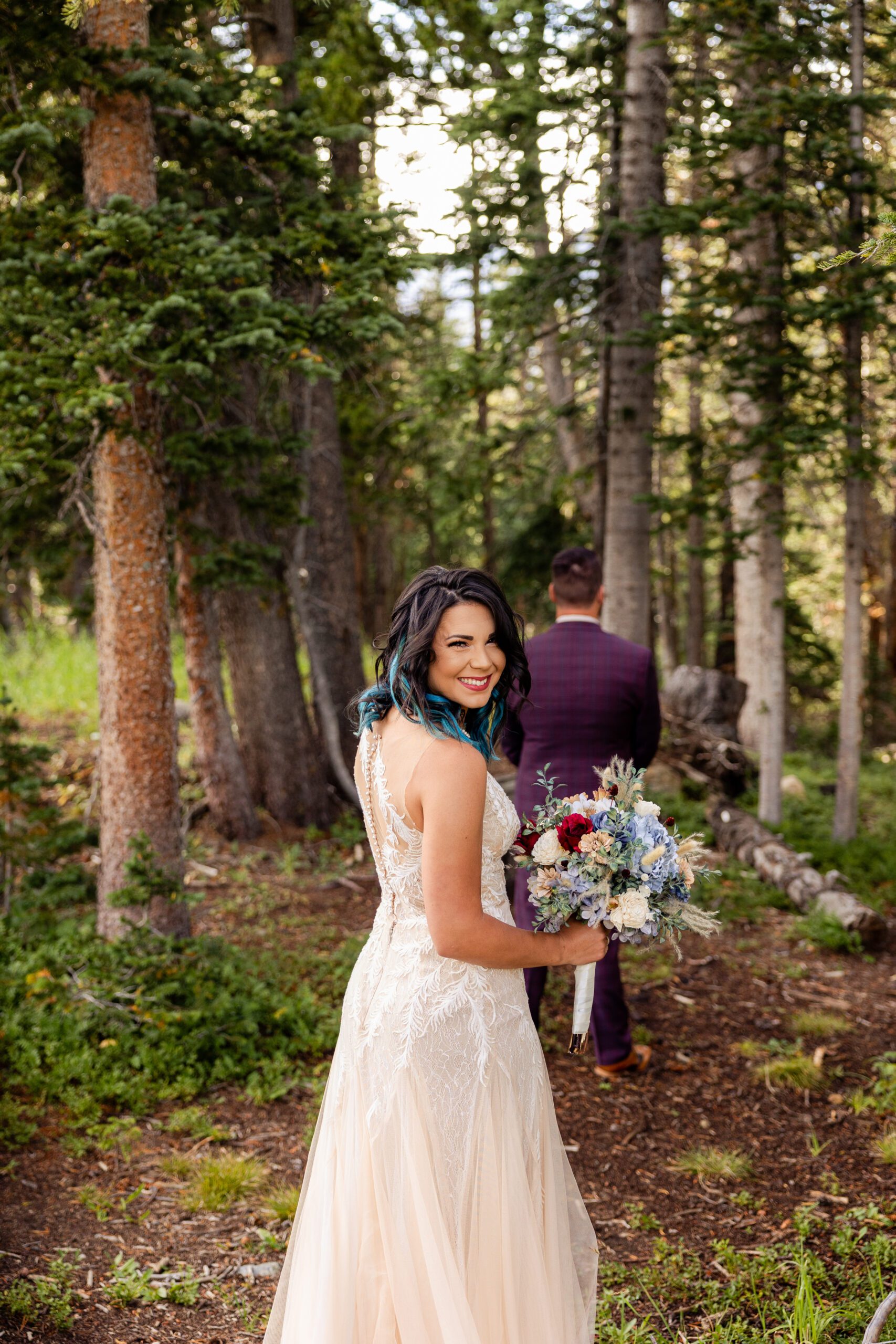 Bride smiles at the camera, groom stands in front of her with his back facing the camera before their first look at their Brainard Lake Elopement.