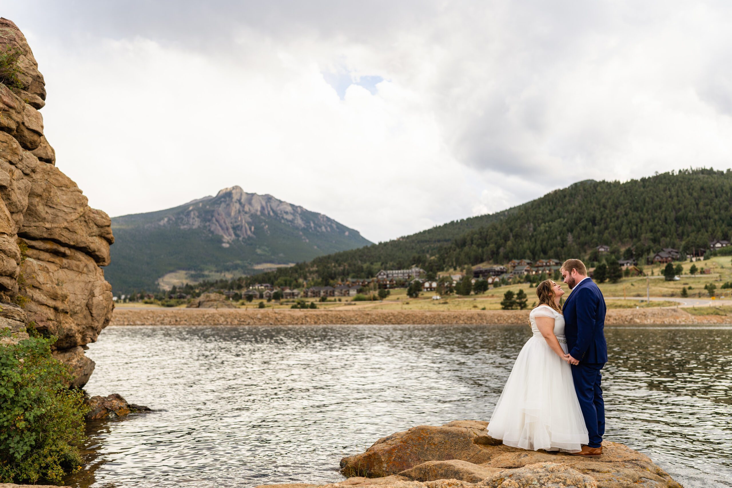 the bride and  groom standing on a rock on the lake, looking at each other at their Bear Lake elopement. 