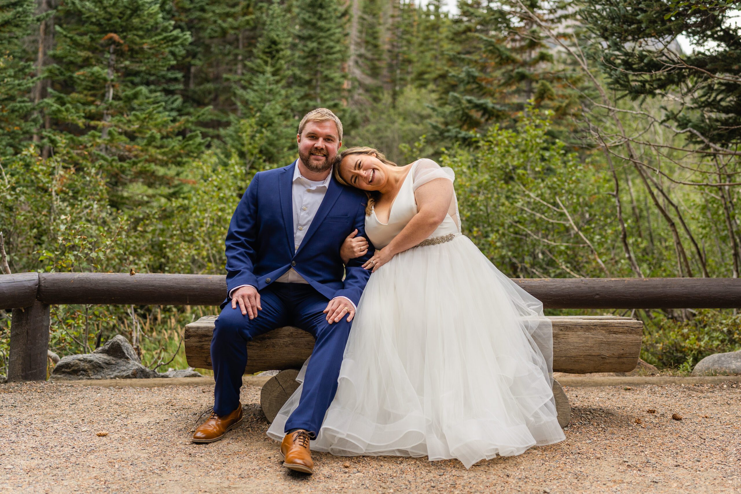 groom and bride sitting down on a bench surrounded by trees, at their Bear Lake elopement. 