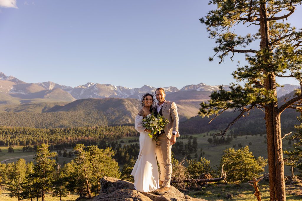 bride and groom standing on a boulder with the sun shining brightly on their skin. it's sunset. 