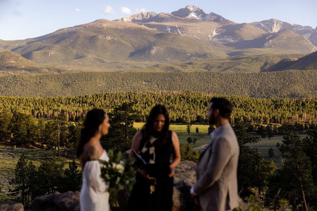 an upclose shot of the bride, groom and their officiant, with a clear view of the rockies behind them. 