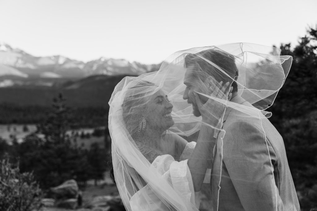 the groom is under the brides veil. it's windy, they are smiling, looking at each other. a black and white image. 