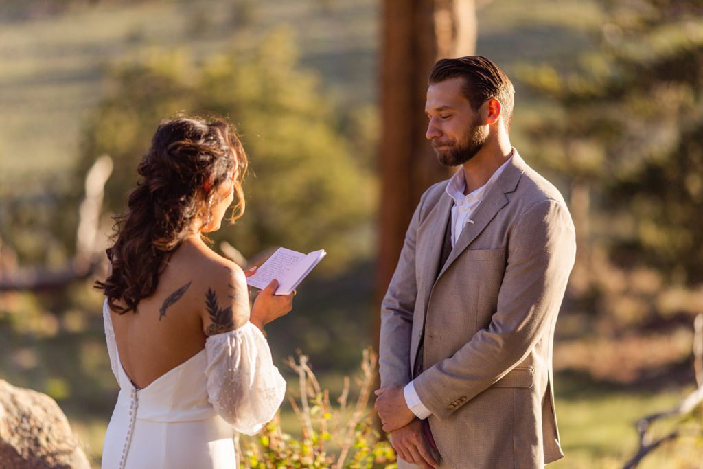 Bride reads vows to her groom, he is emotional and smiling 