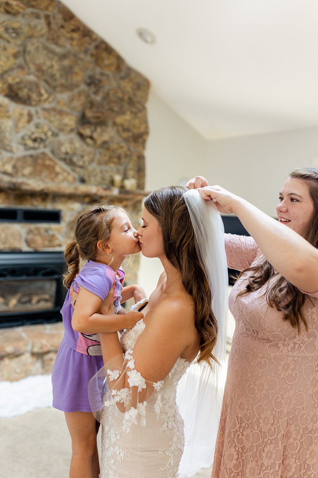 The beautiful bride kisses her little girl while getting ready, wearing her wedding dress.
