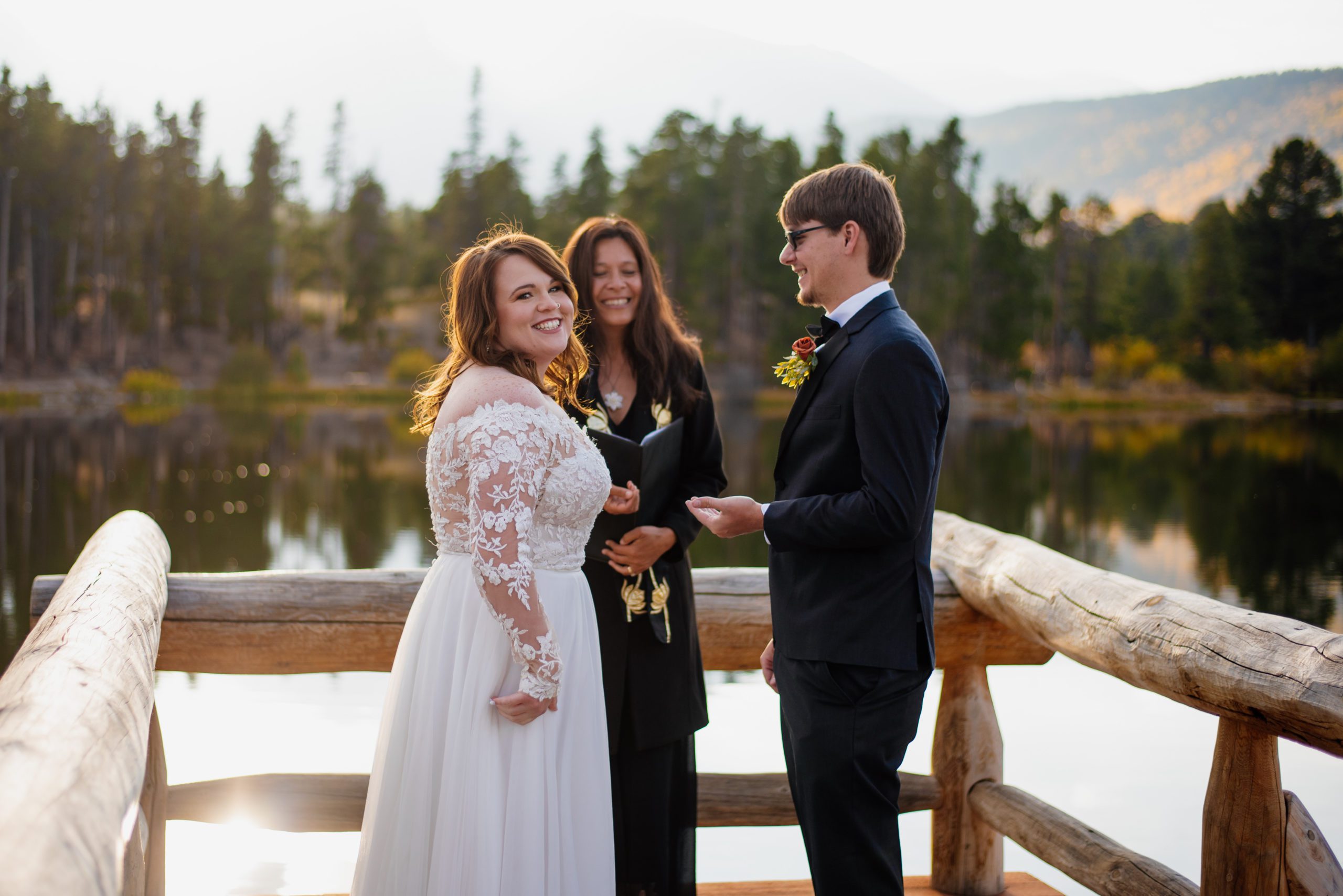 bride smiles at camera - groom and officiant smile in the background at Sprague Lake - RMNP
