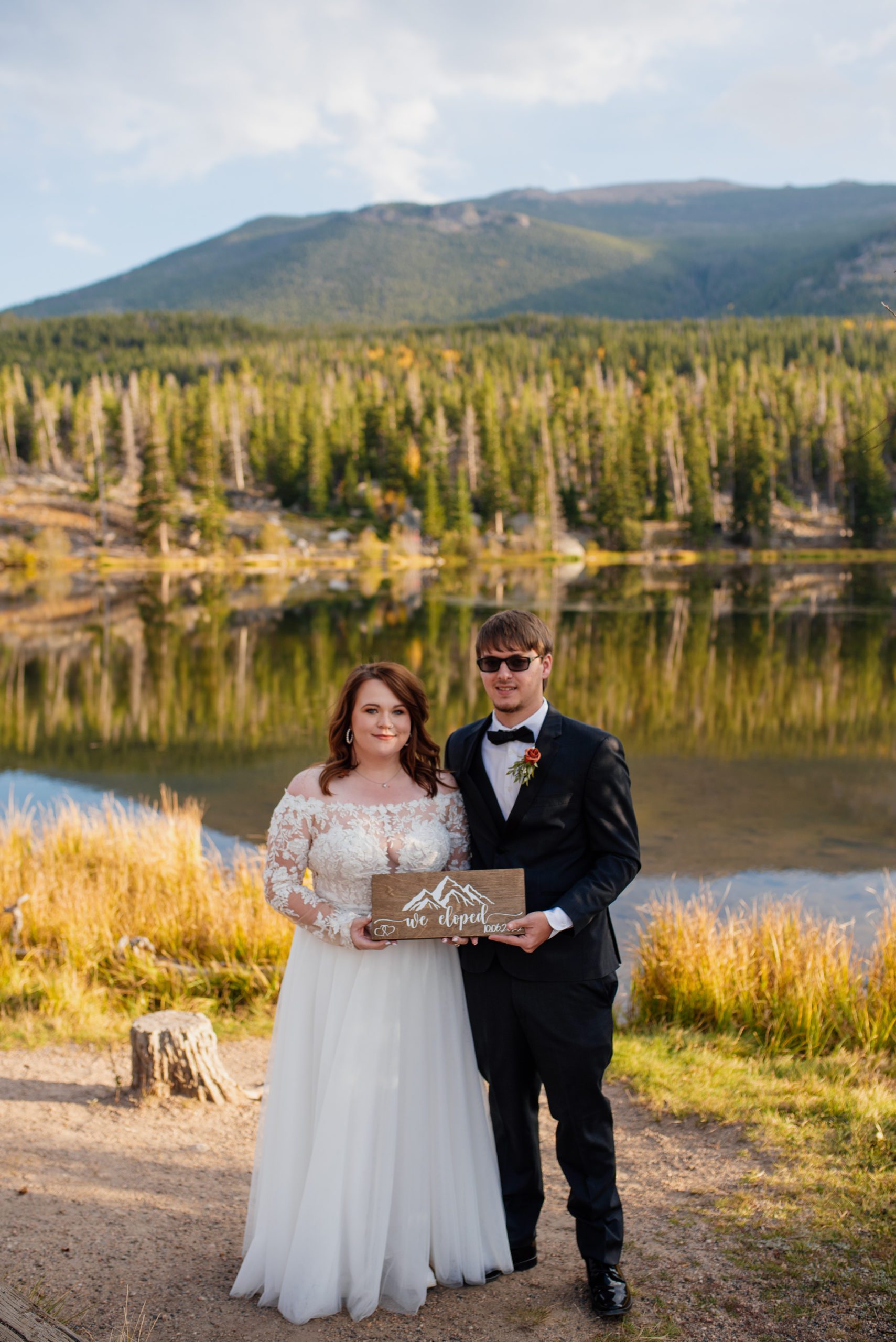 Bride and groom hold a "just eloped" sign in front of the lake at Sprague Lake - RMNP
