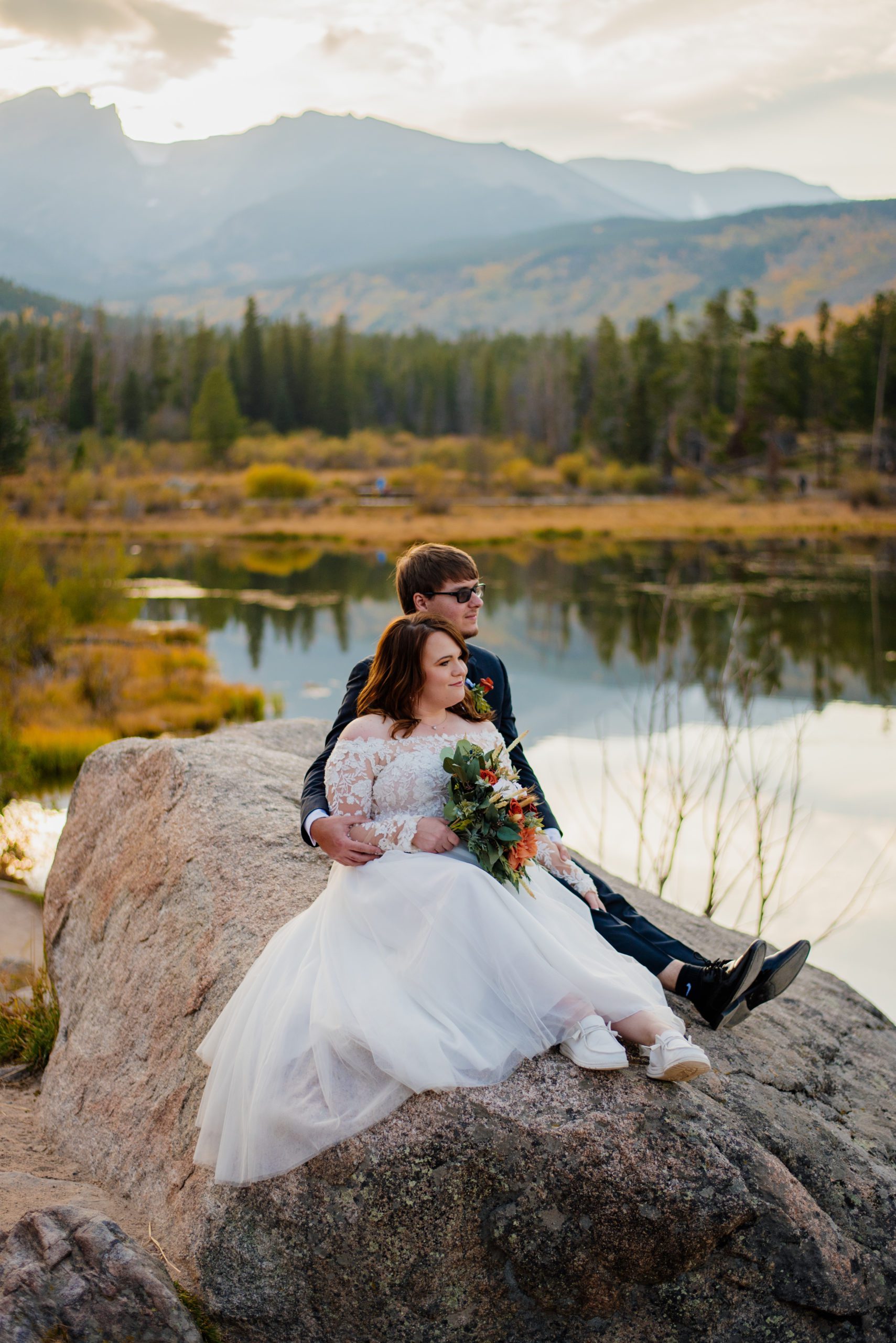 Bride and groom looking off at the distance - sitting on a rock at Sprague Lake - RMNP