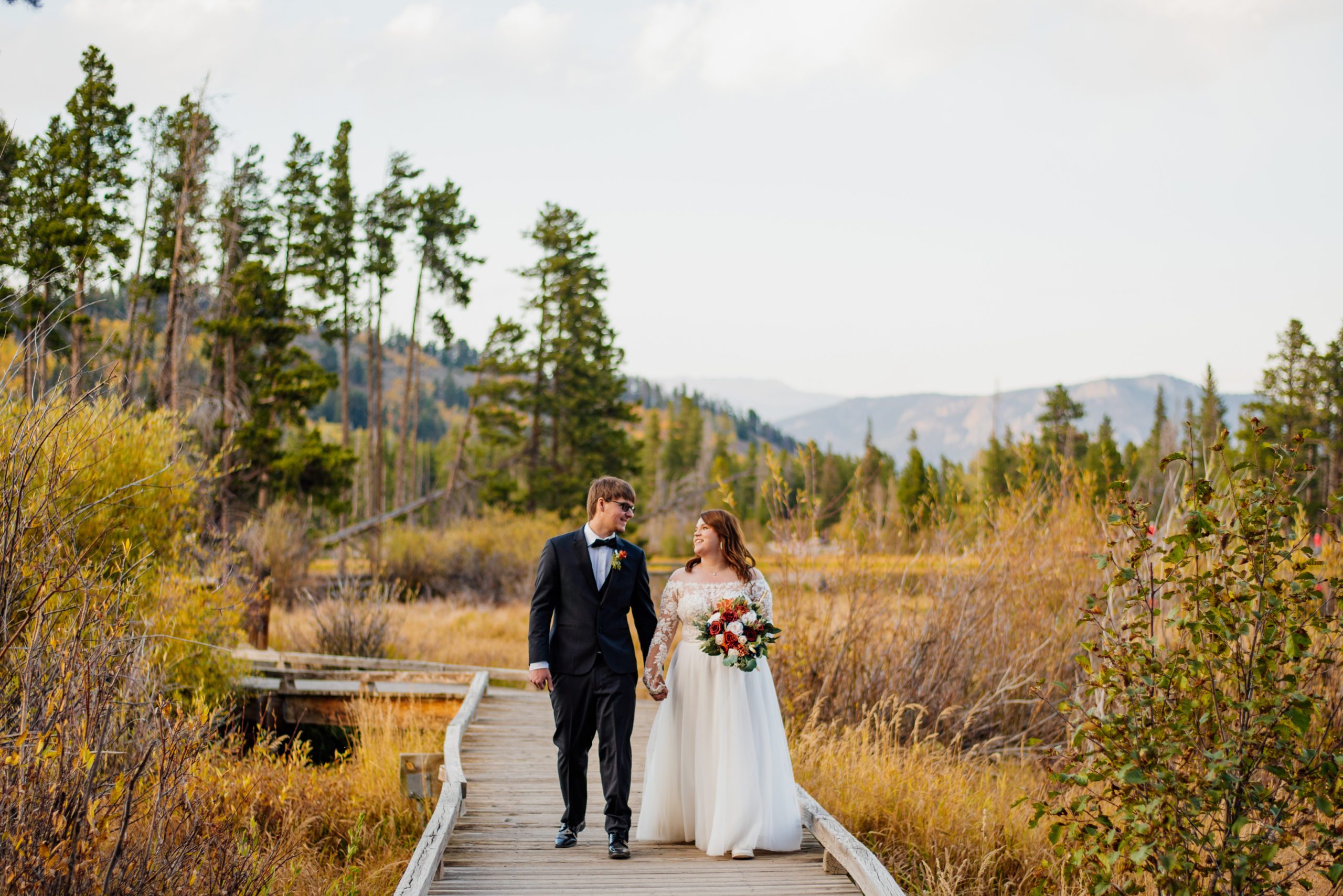 Bride and groom holding hands together walking at Sprague Lake - RMNP