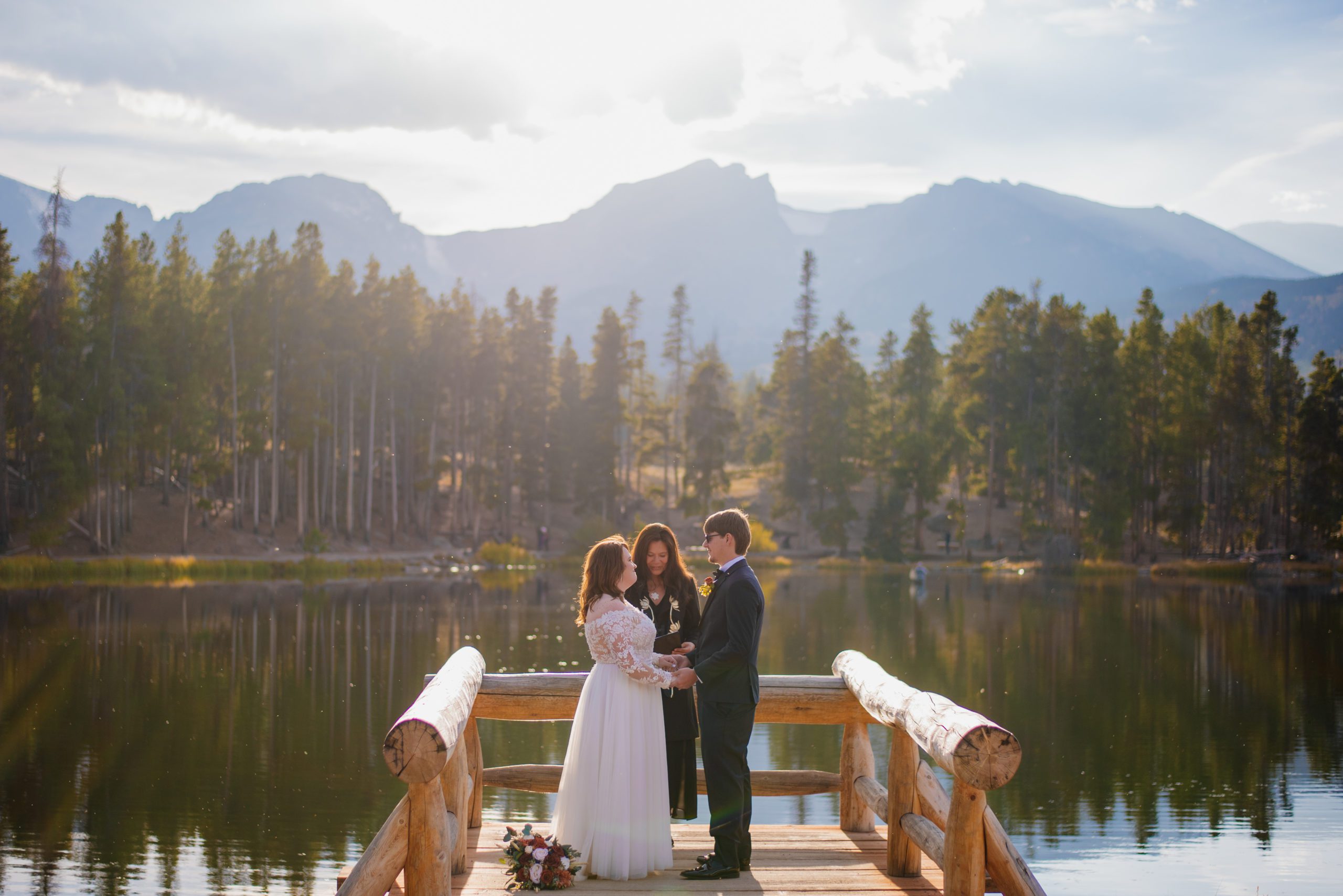 Bride and groom look lovingly at each other holding hands on the lake
at Sprague Lake - RMNP