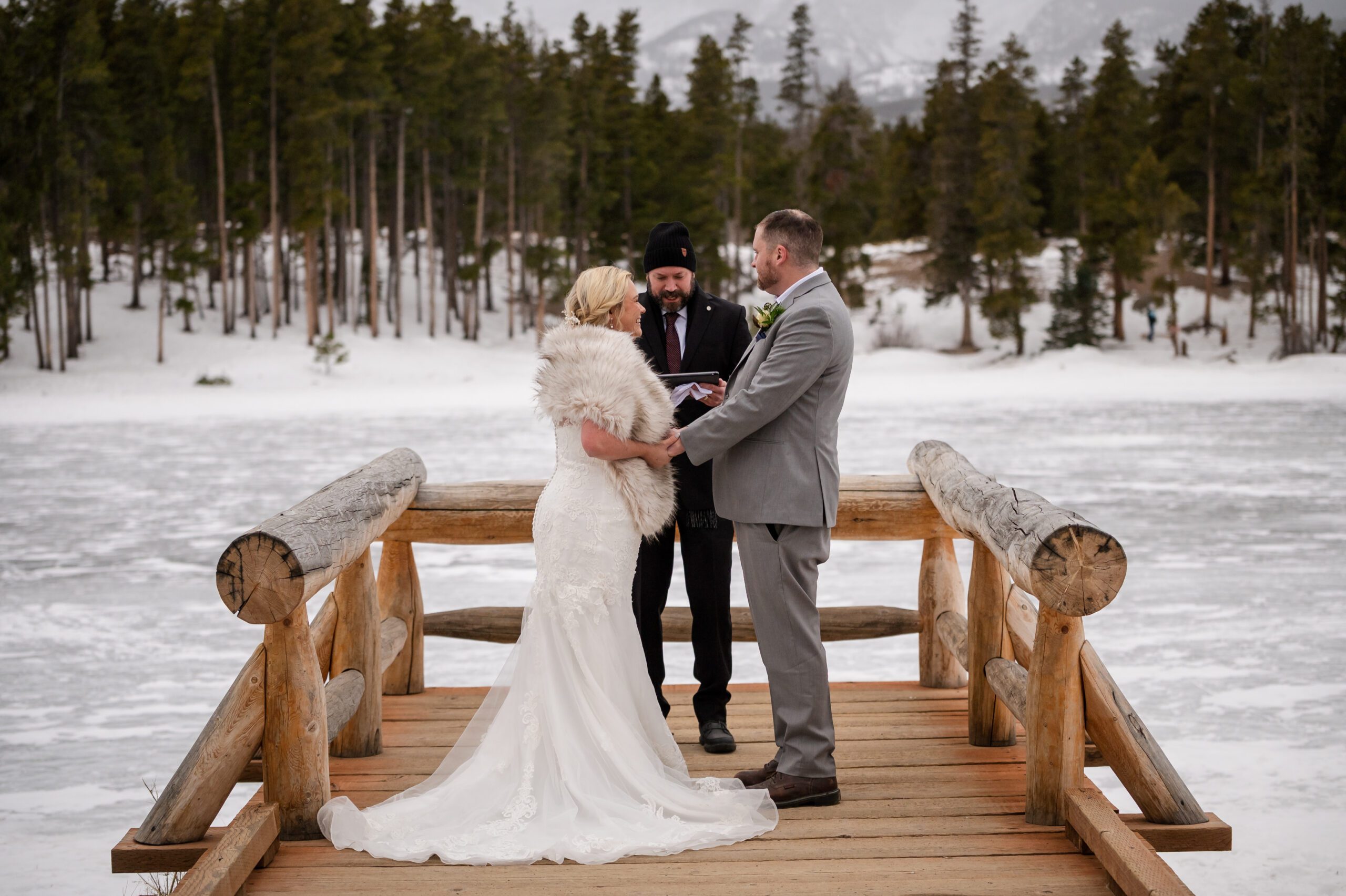 the bride smiles as she hodls her grooms hands during their Winter Elopement ceremony at Sprague Lake.  