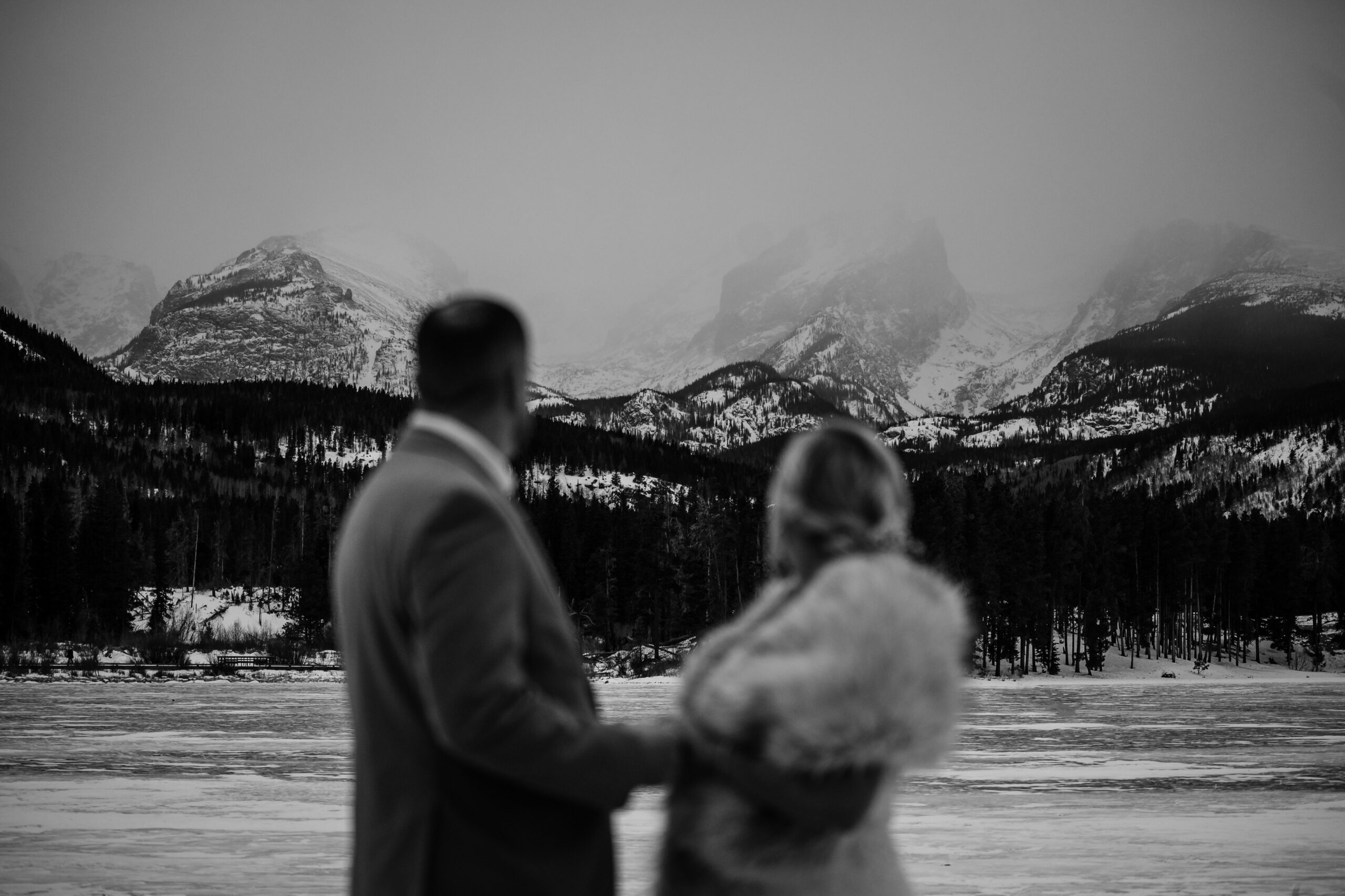 a black and white photo of the bride and groom looking out on the mountain range during their Winter Elopement at Sprague Lake. 
