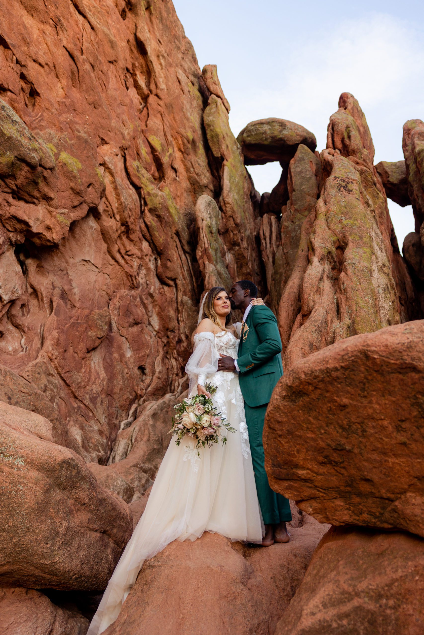 Groom kisses bride on the cheek at the Garden of the Gods. 