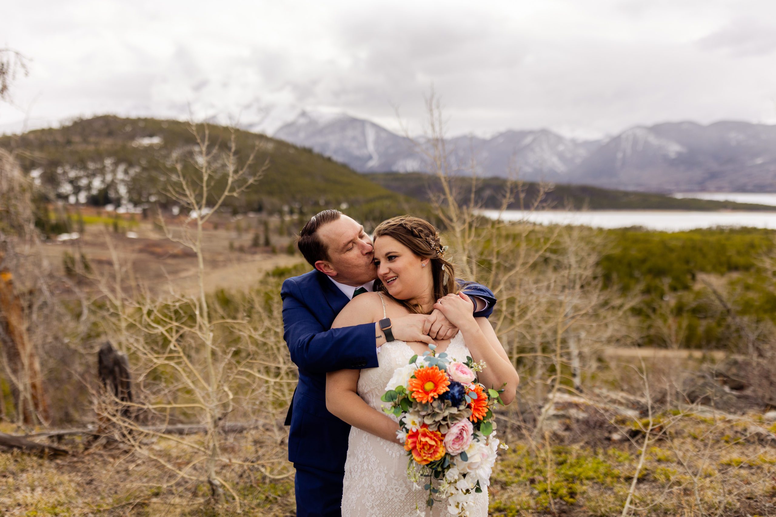 The groom kisses his bride while she smiles on their Sapphire Point Elopement day. 