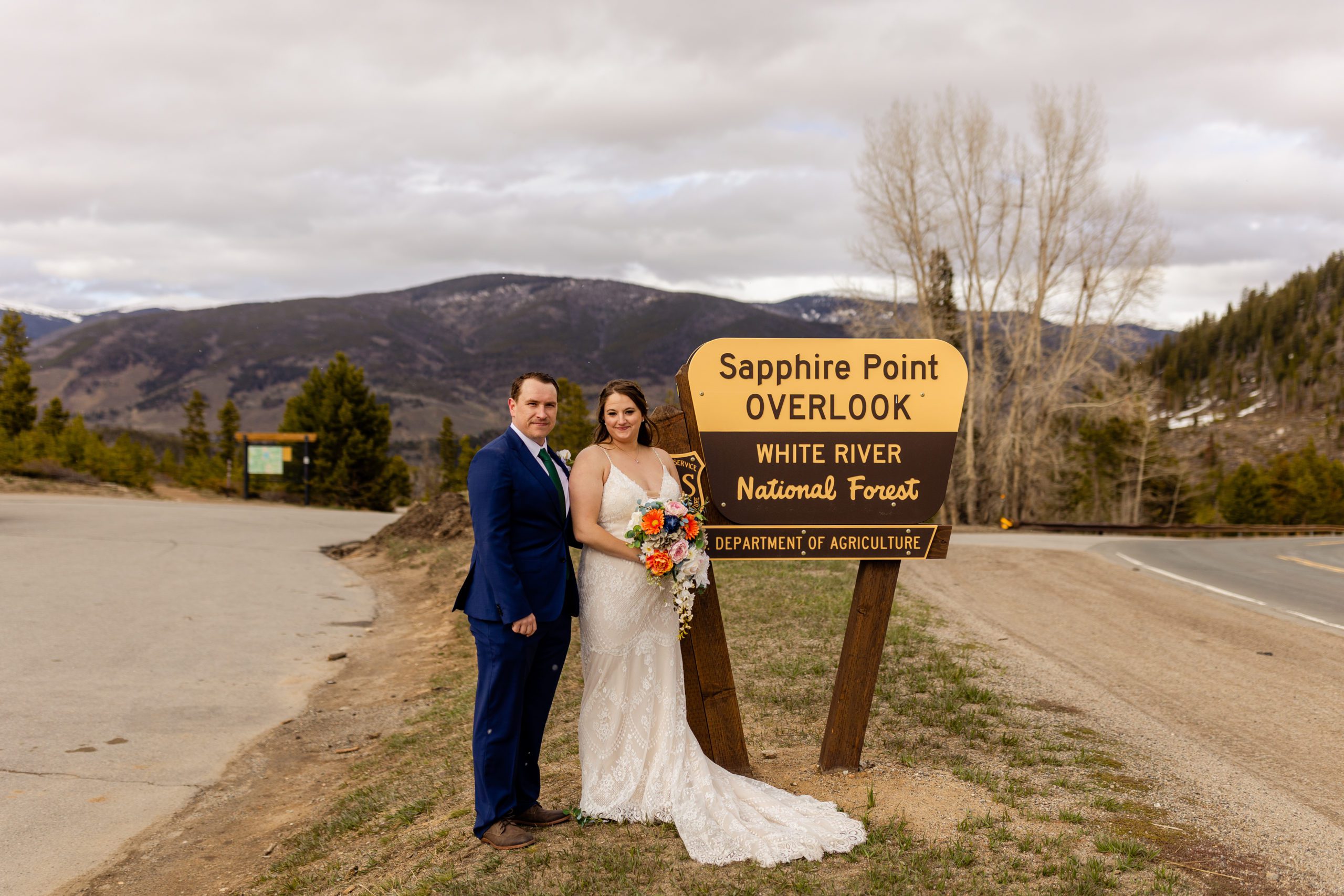 The bride and groom at their Sapphire Point Elopement, standing by the national forest sign. 
