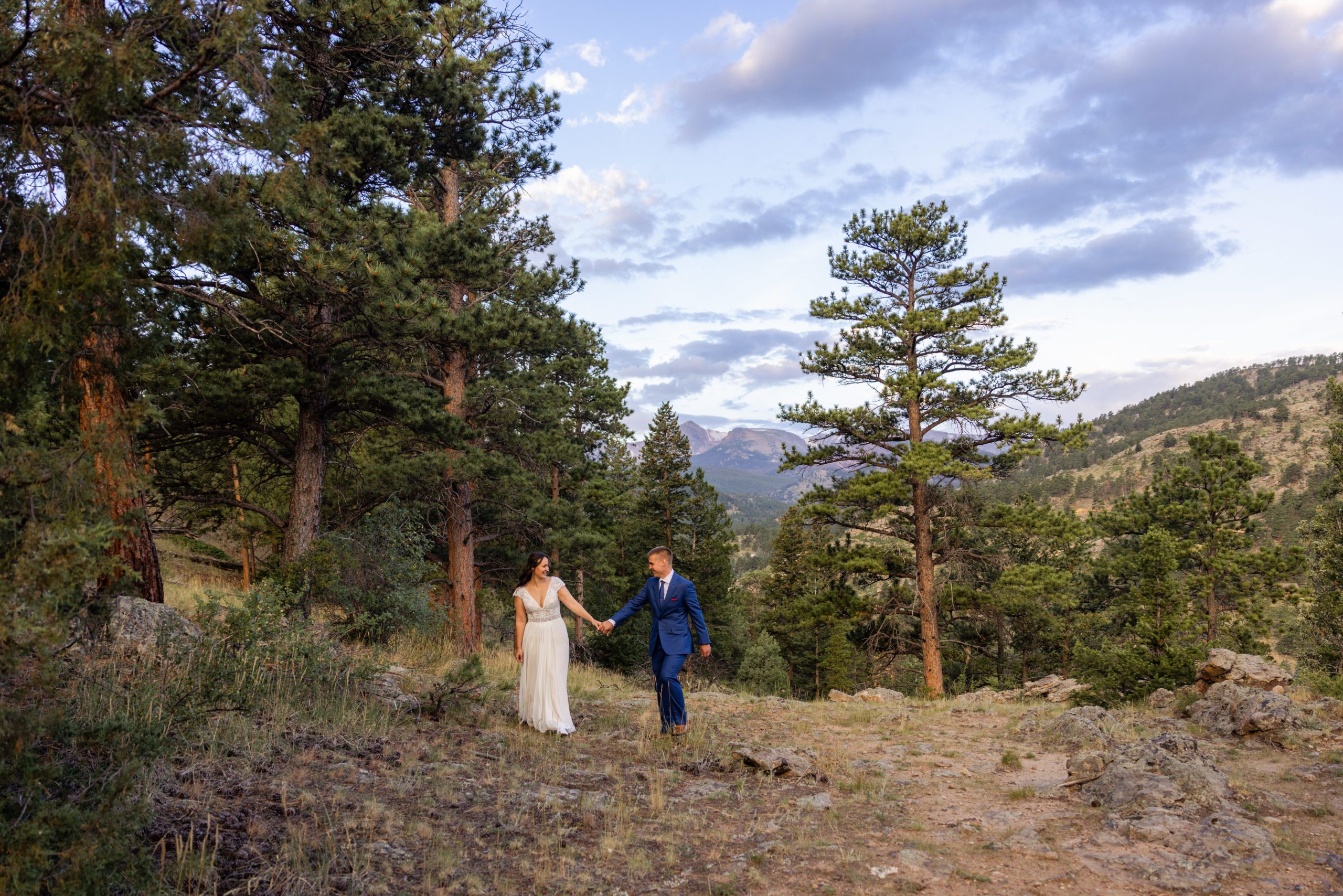 bride and groom walk hand in hand at on a nearby trail from Romantic RiverSong Inn in Estes Park on their wedding day.