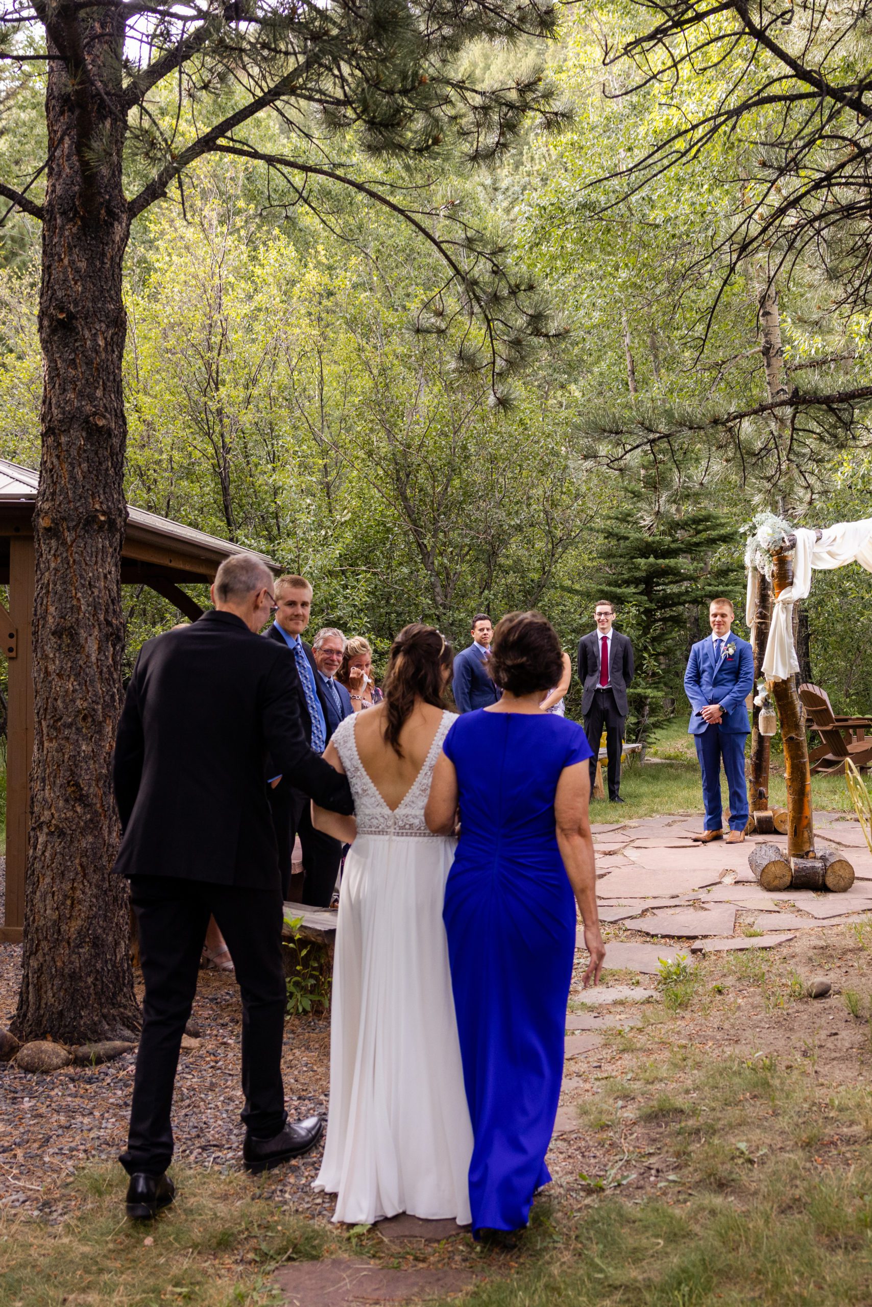 The bride walks down the aisle with her parents towards her groom at Romantic RiverSong Inn in Estes Park during their wedding. 