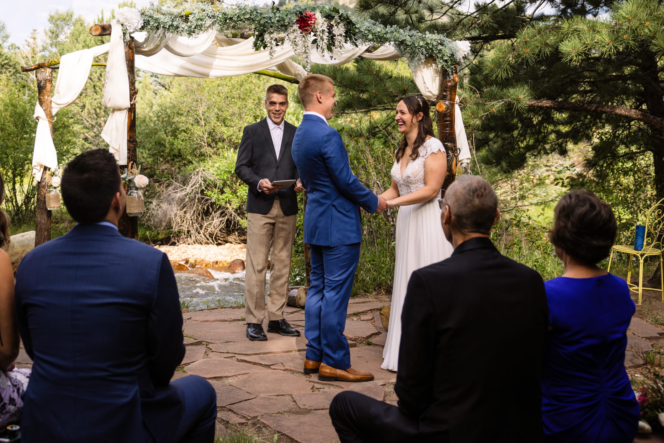 The bride smiles at her groom as the officiant gives a welcome speech at Romantic RiverSong Inn in Estes Park on their wedding day. 