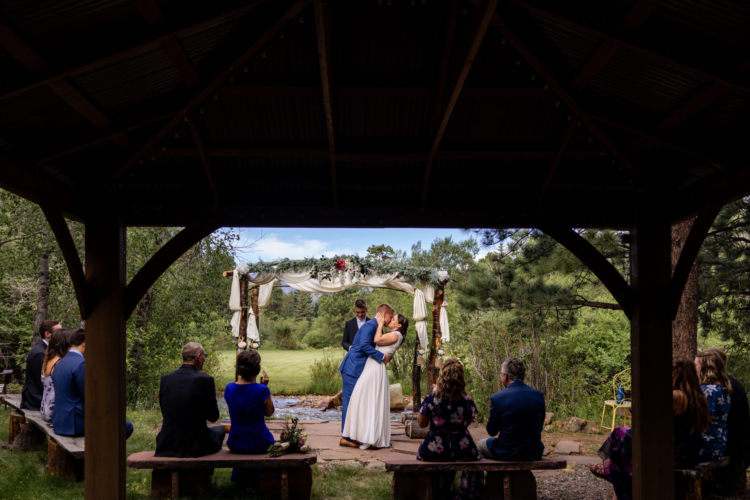 A photo of the entire wedding as the bride and groom kiss at their wedding at Romantic RiverSong Inn in Estes Park. 