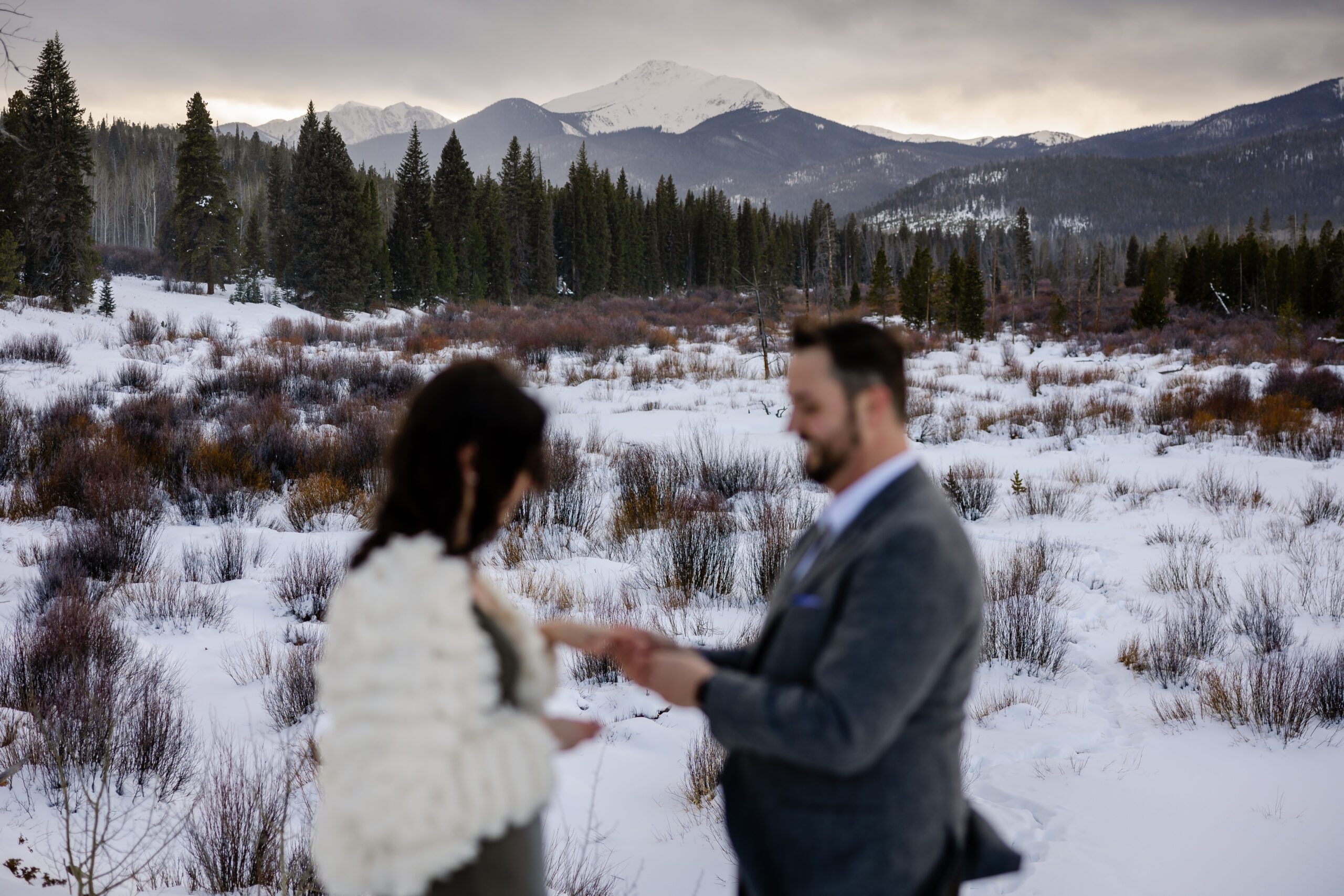 a blurry shot of the couple with an in focus shot of the mountain in the background at their Winter Park elopement ceremony. 