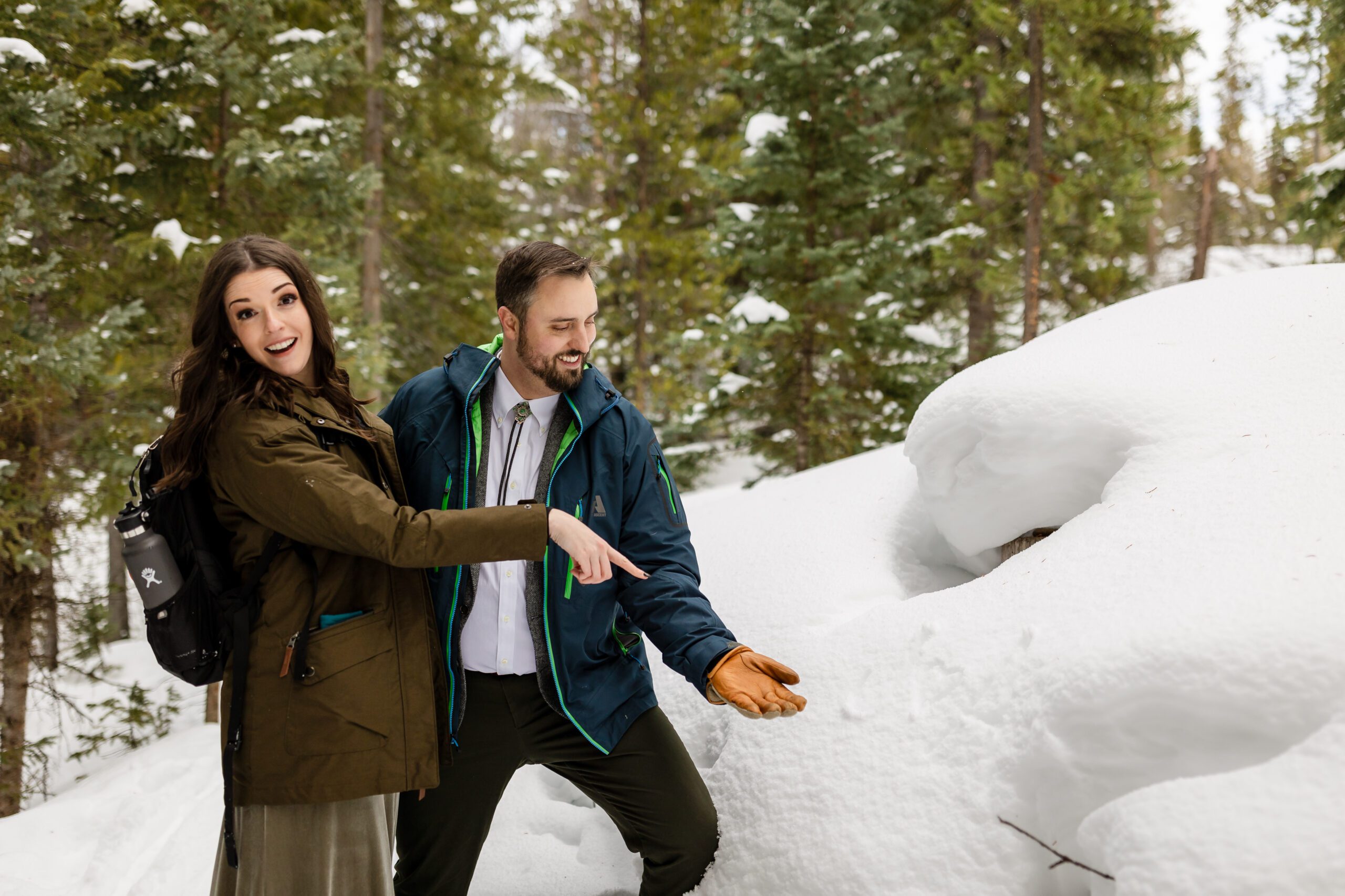 bride and groom pointing at the snow, looking at the camera, during  their Winter Park elopement.