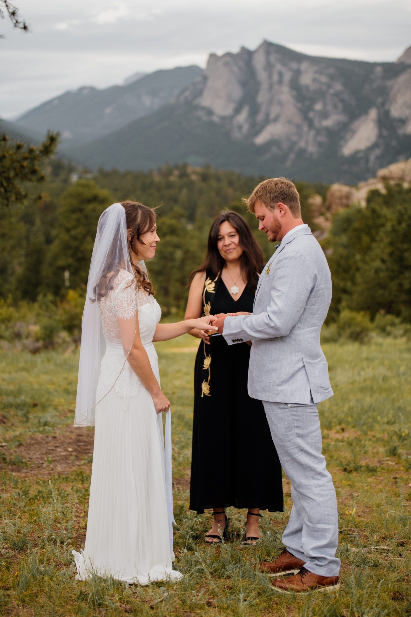 The groom places the ring on his wife's hand during their elopement ceremony at Knoll Willows in Estes Park.
