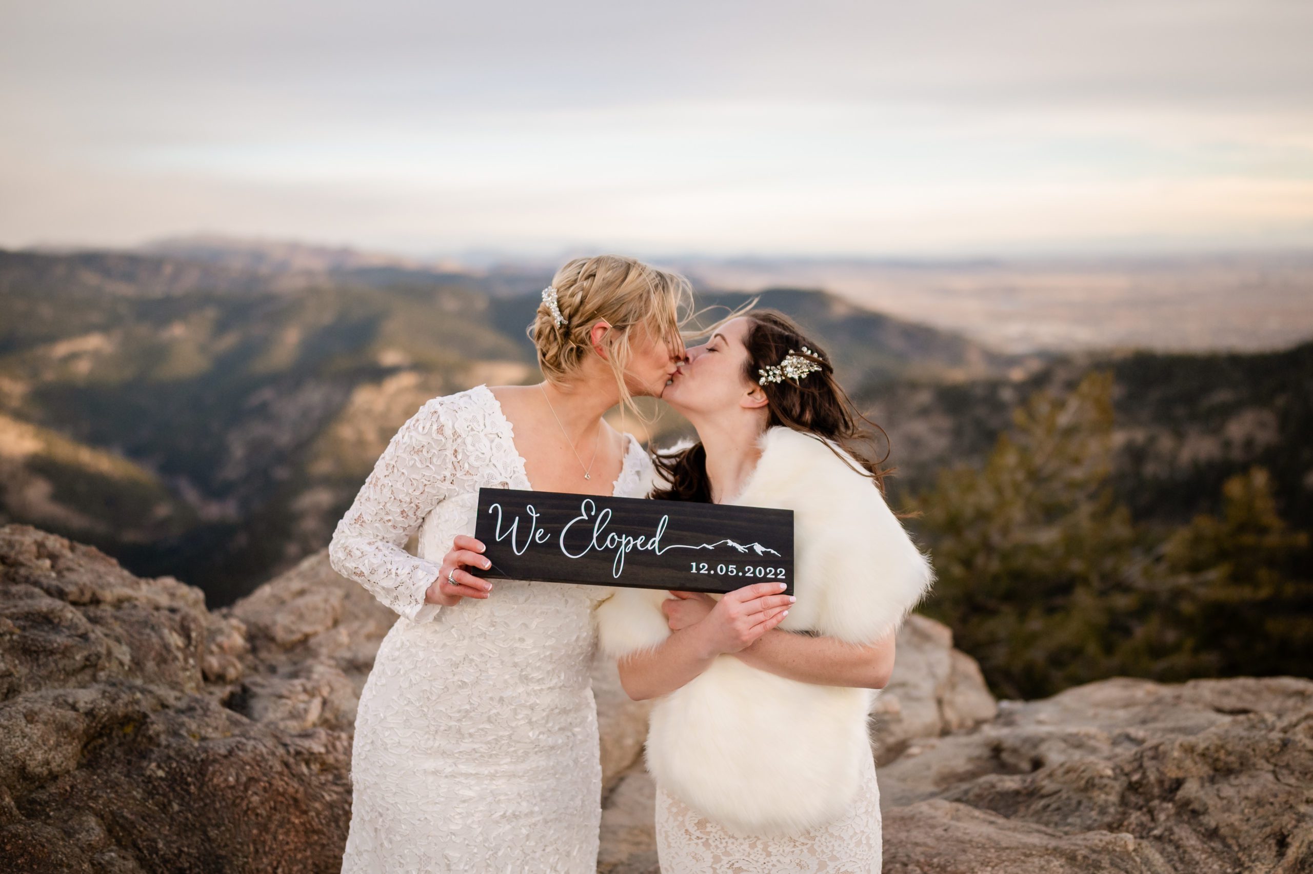The brides kiss while holding their "we eloped" sign at their Lost Gulch Elopement 