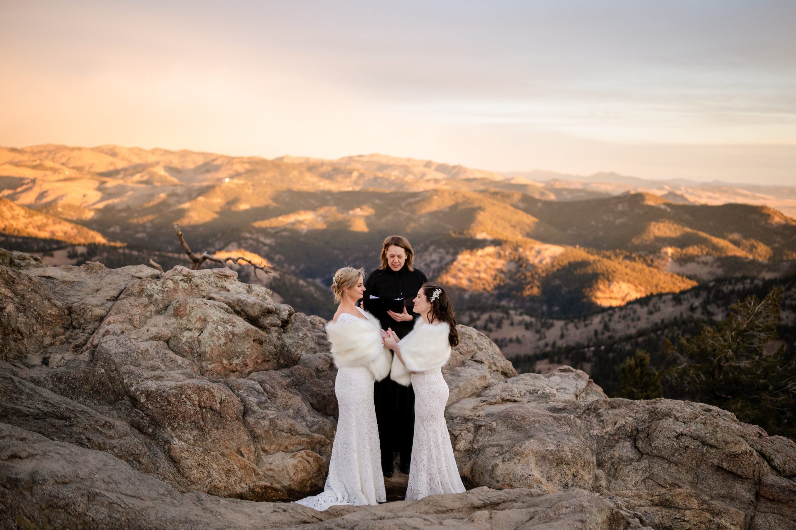The two brides holding hands as the officiant leads them during their Lost Gulch elopement ceremony. 