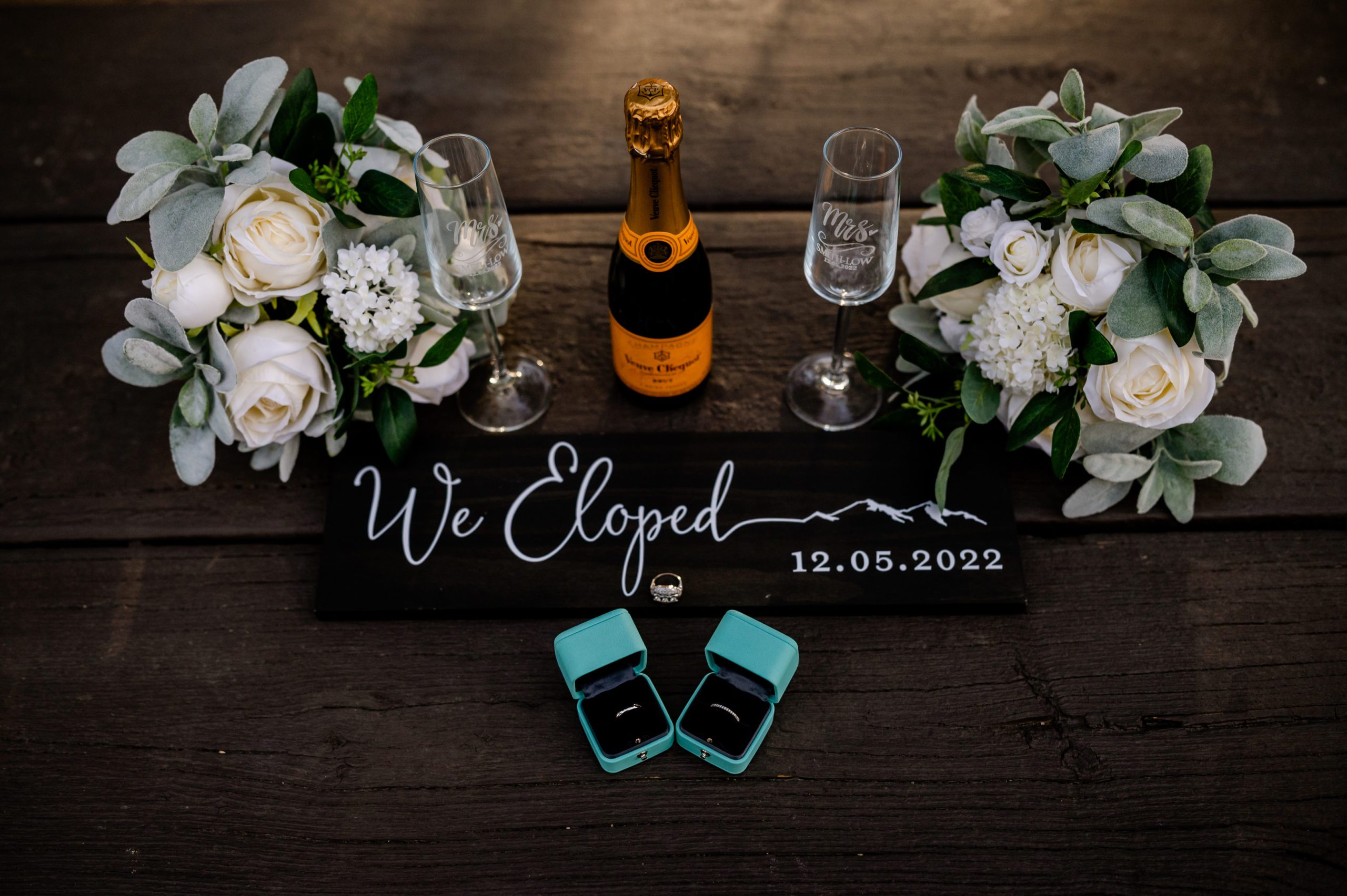 A detailed shot of their flowers, 'we eloped' sign, Tiffany rings, and Champagne at their Lost Gulch elopement. 