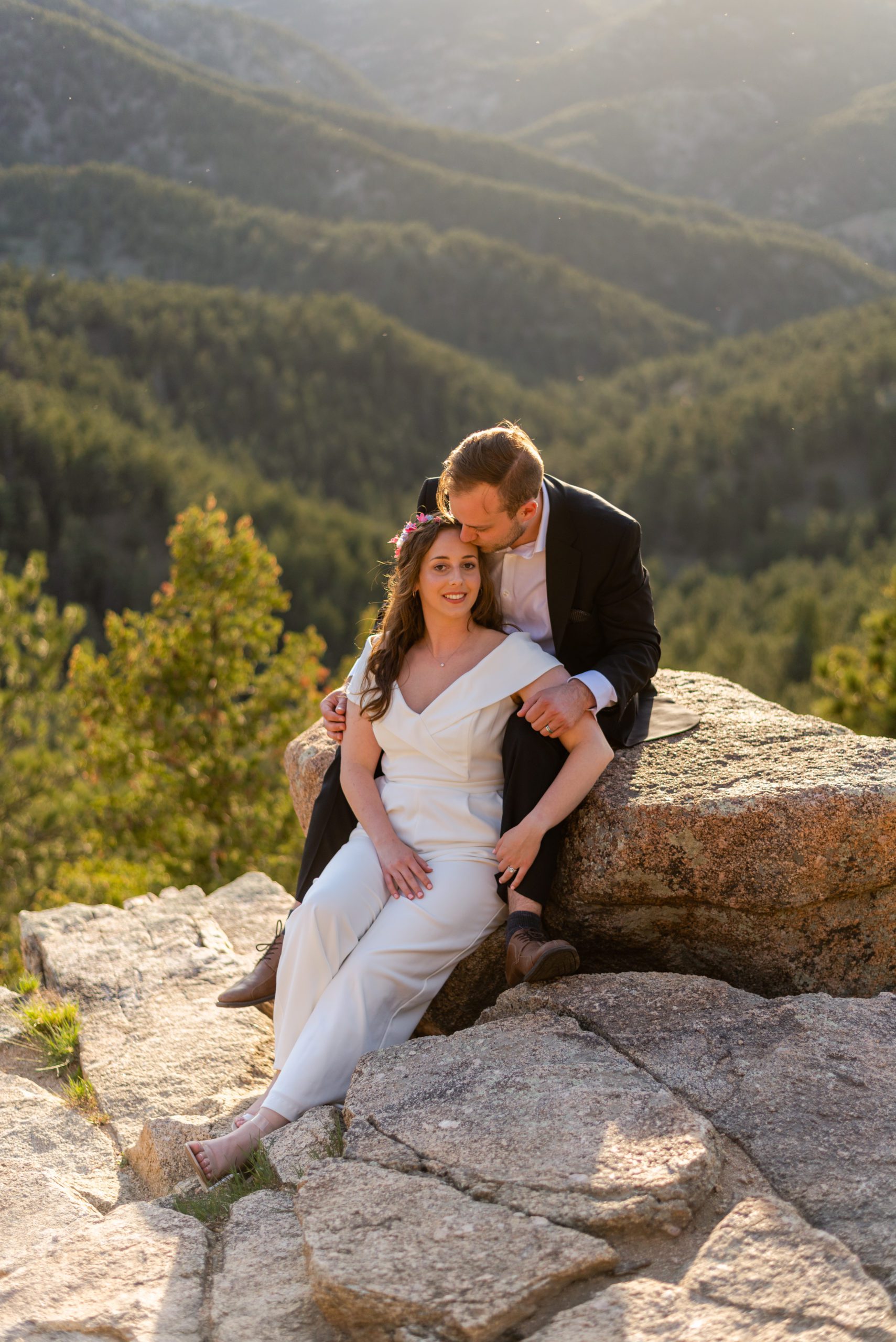 The groom kisses his bride on the forehead as she sits between his legs at the overlook during their Boulder hiking elopement near realization point.