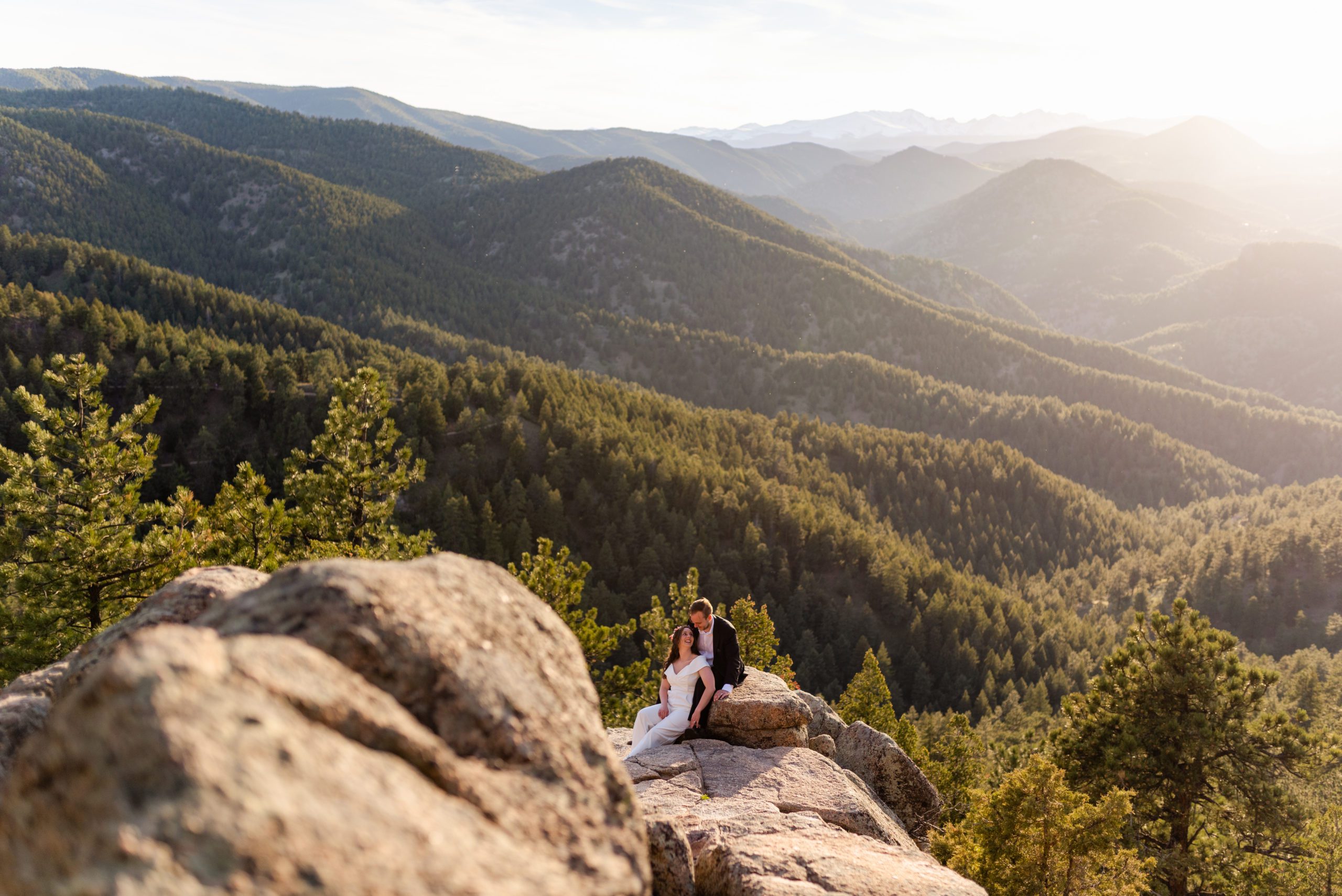 A shot of the couple among the gorgeous green valley of tress below during their Boulder hiking elopement near realization point.
