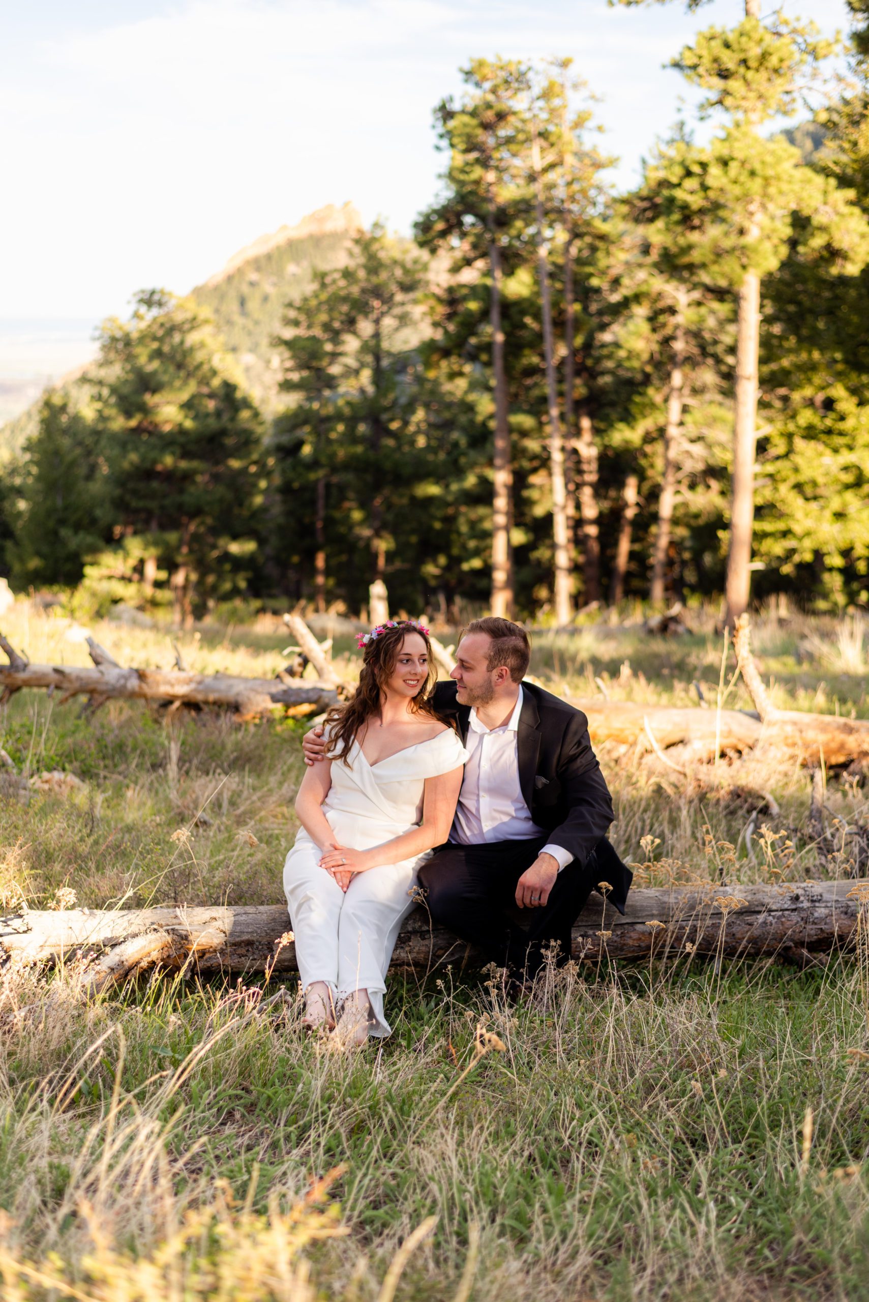 The bride smiles sweetly at her groom while they sit together on a log during their Boulder hiking elopement near realization point.