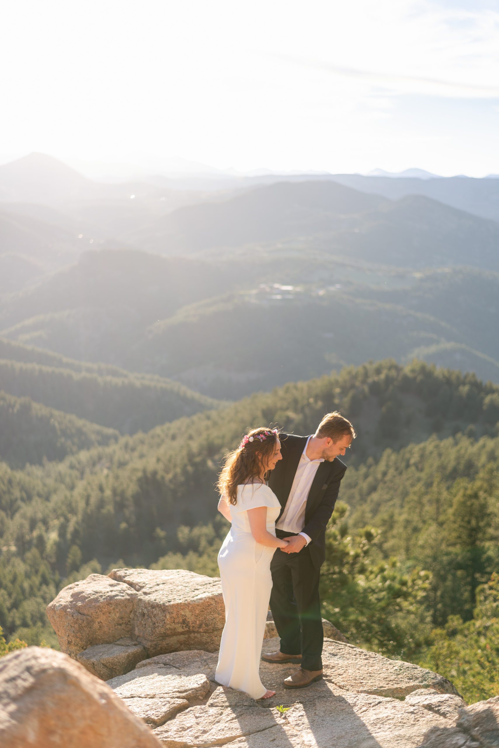 The bride and groom hold hands while looking down below the overlook during their Boulder hiking elopement near realization point.