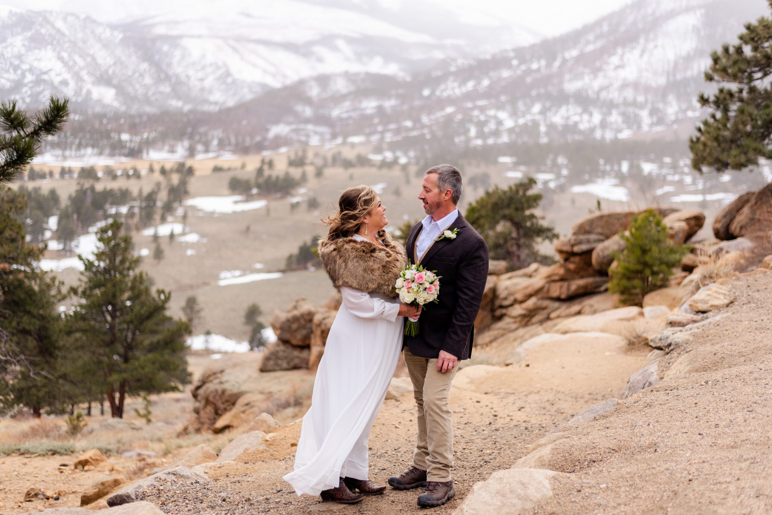 the bride and groom smile at each other, the gorgeous white covered mountains in the distance during their  spring  elopement at 3M Curve.