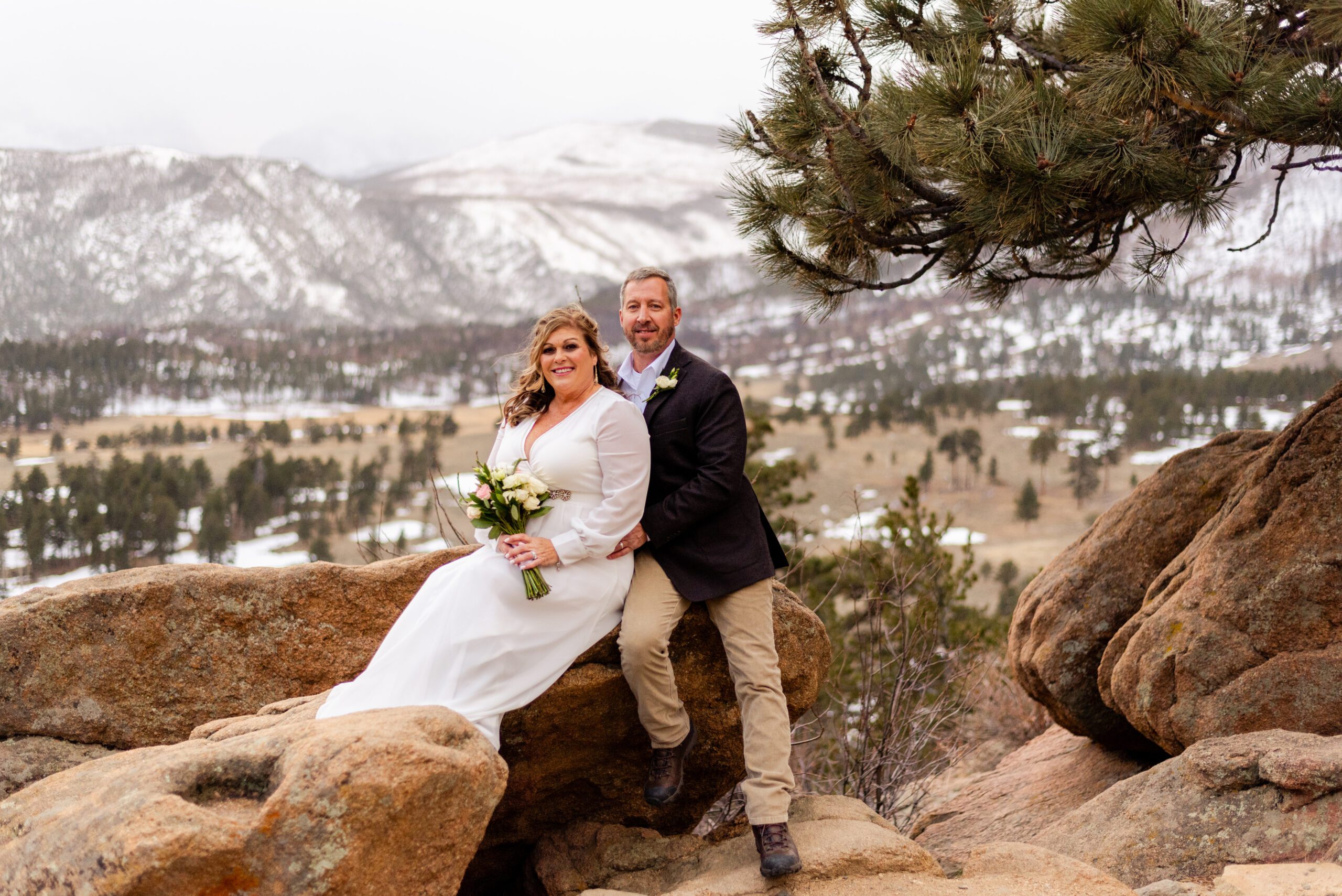 bride and groom sitting on a rock with the beautiful mountains in the distance during their spring  elopement at 3M Curve.