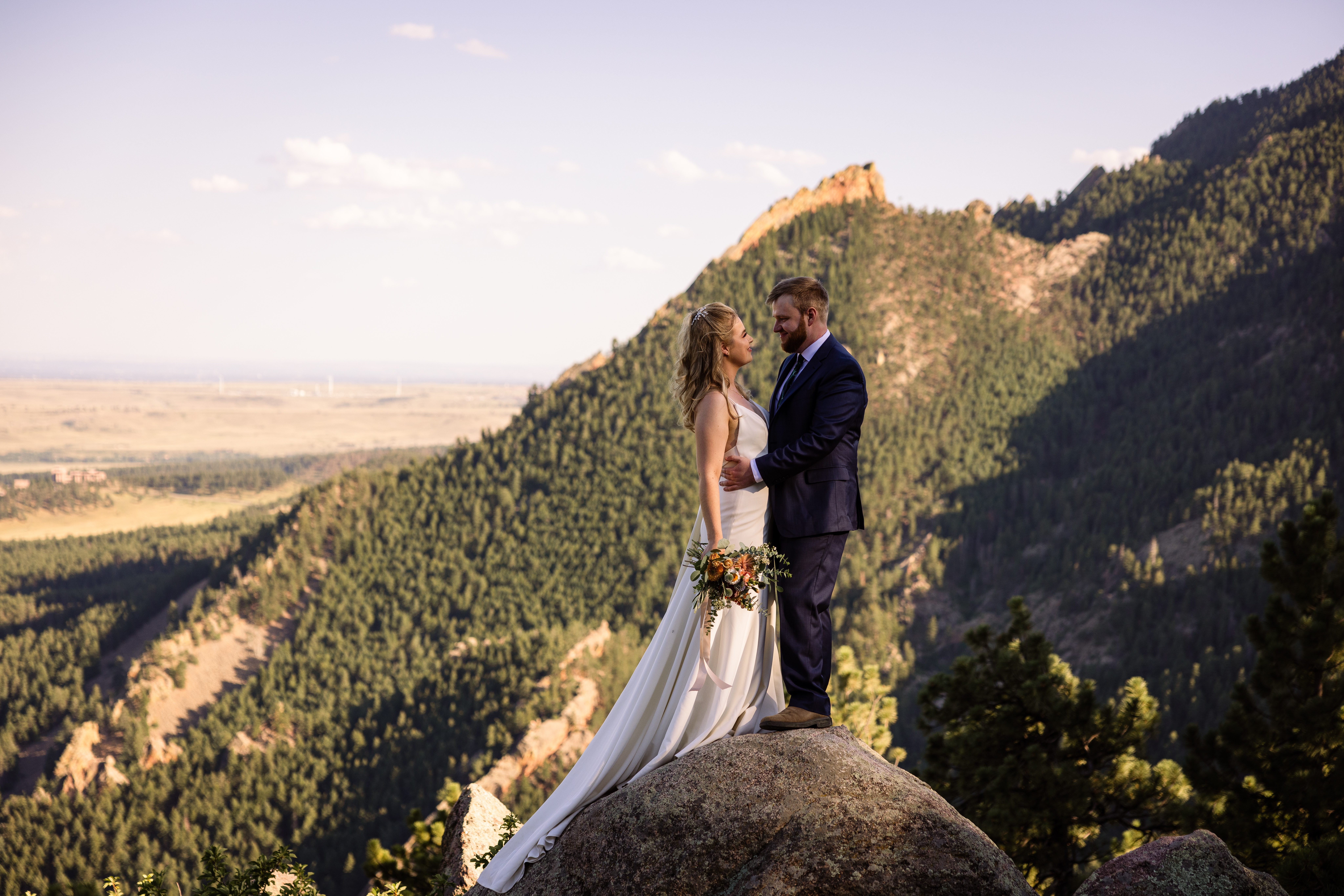 the bride and groom standing on a huge boulder near Sunrise Amphitheater after their wedding.