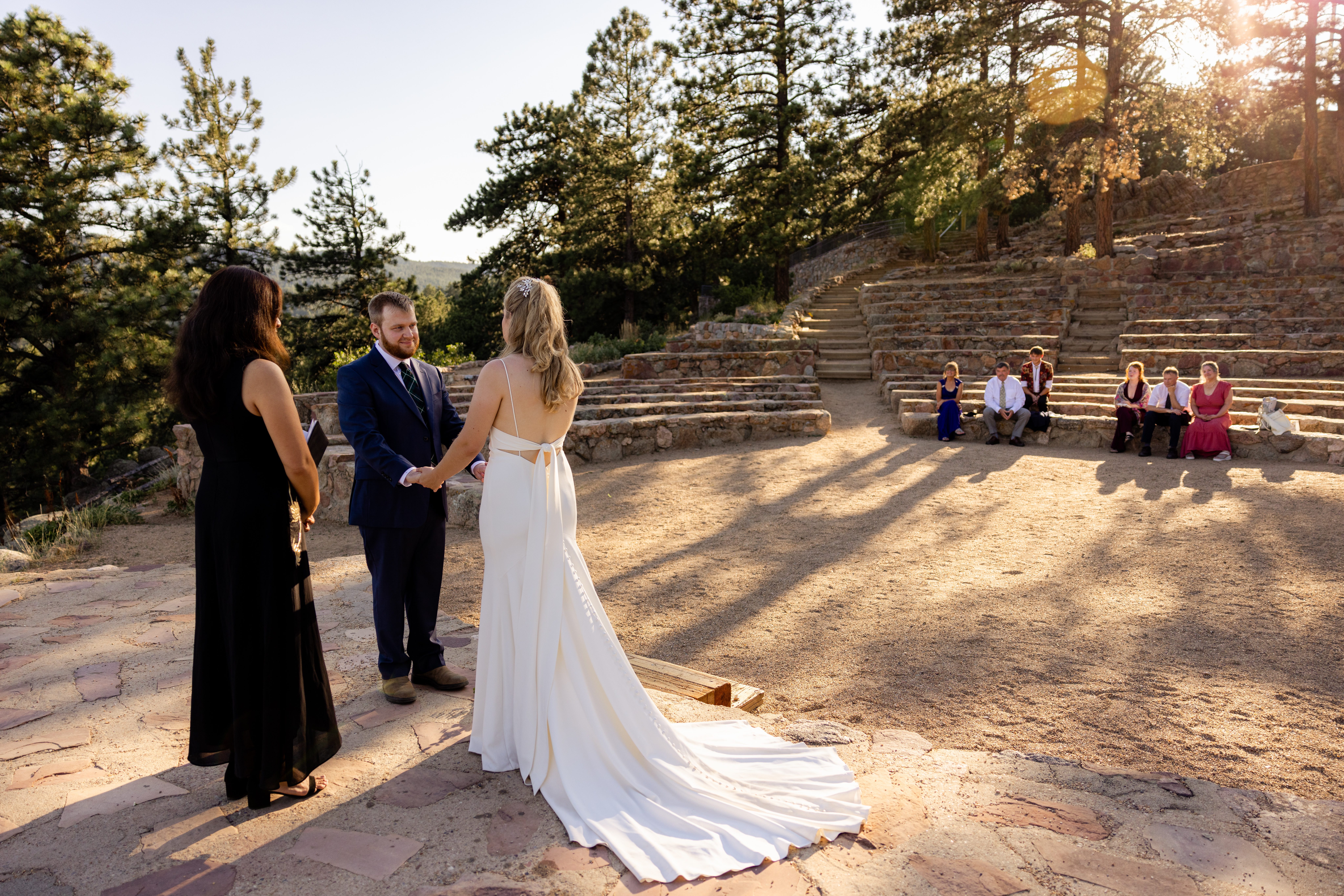 The bride and groom holding hands during their ceremony, with their guests watching in the distance at their Sunrise Amphitheater wedding.