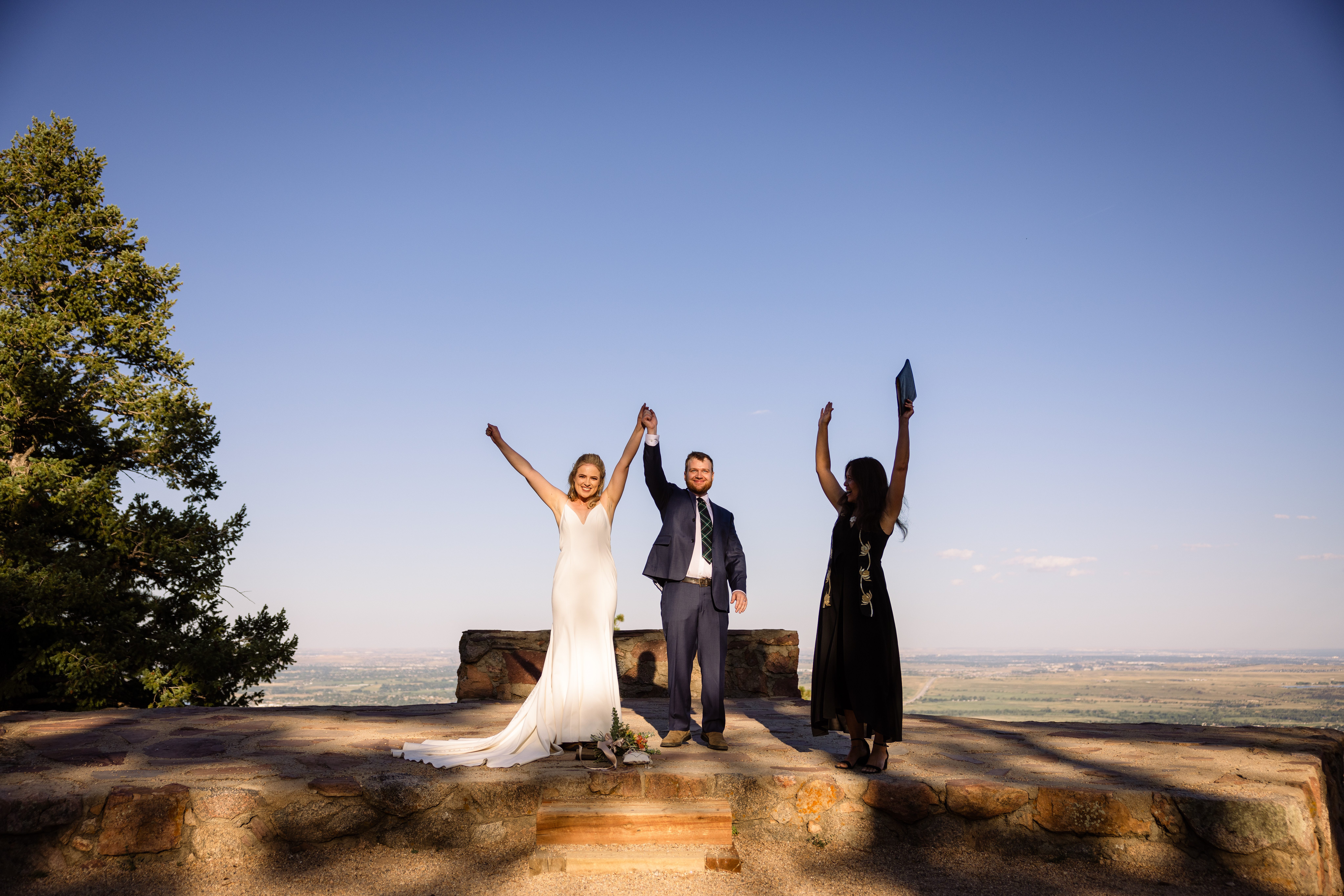 The bride and groom raise their hands in celebration with their officiant at their Sunrise Amphitheater wedding.