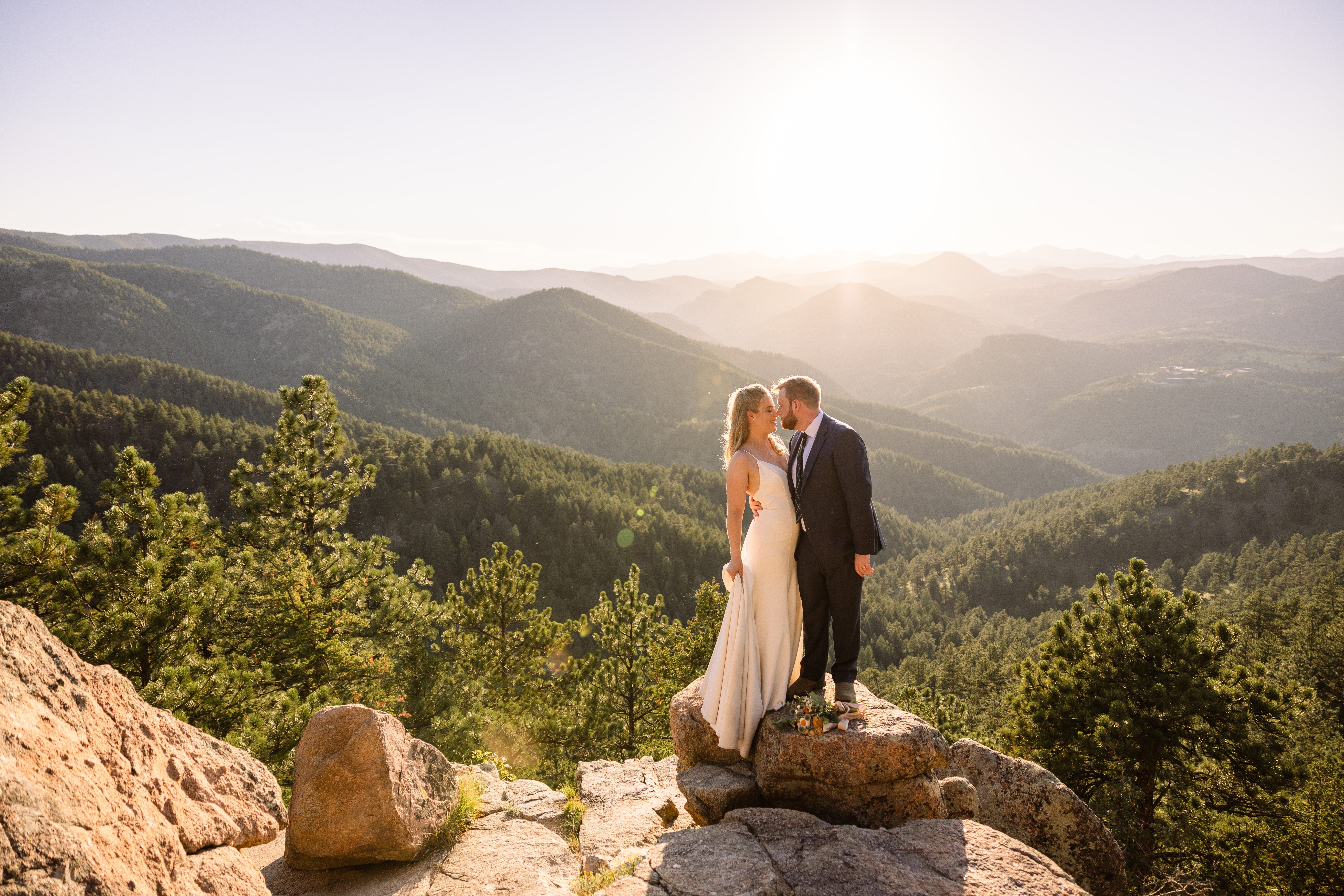 The bride and groom standing on a mountain stop nose to nose after their Sunrise Amphitheater wedding.