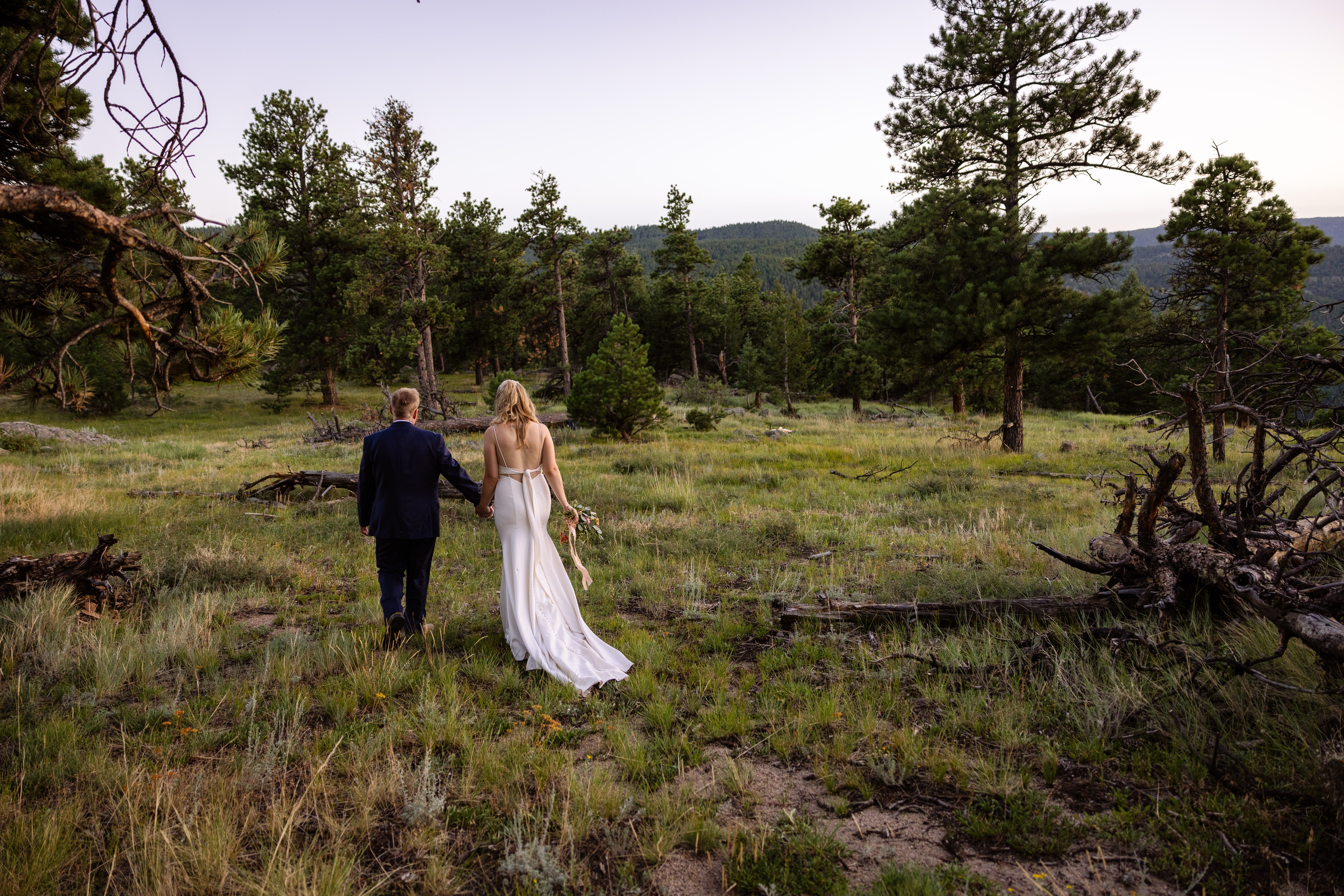 the bride and groom walking together in a meadow near Sunrise Amphitheater on their wedding day.