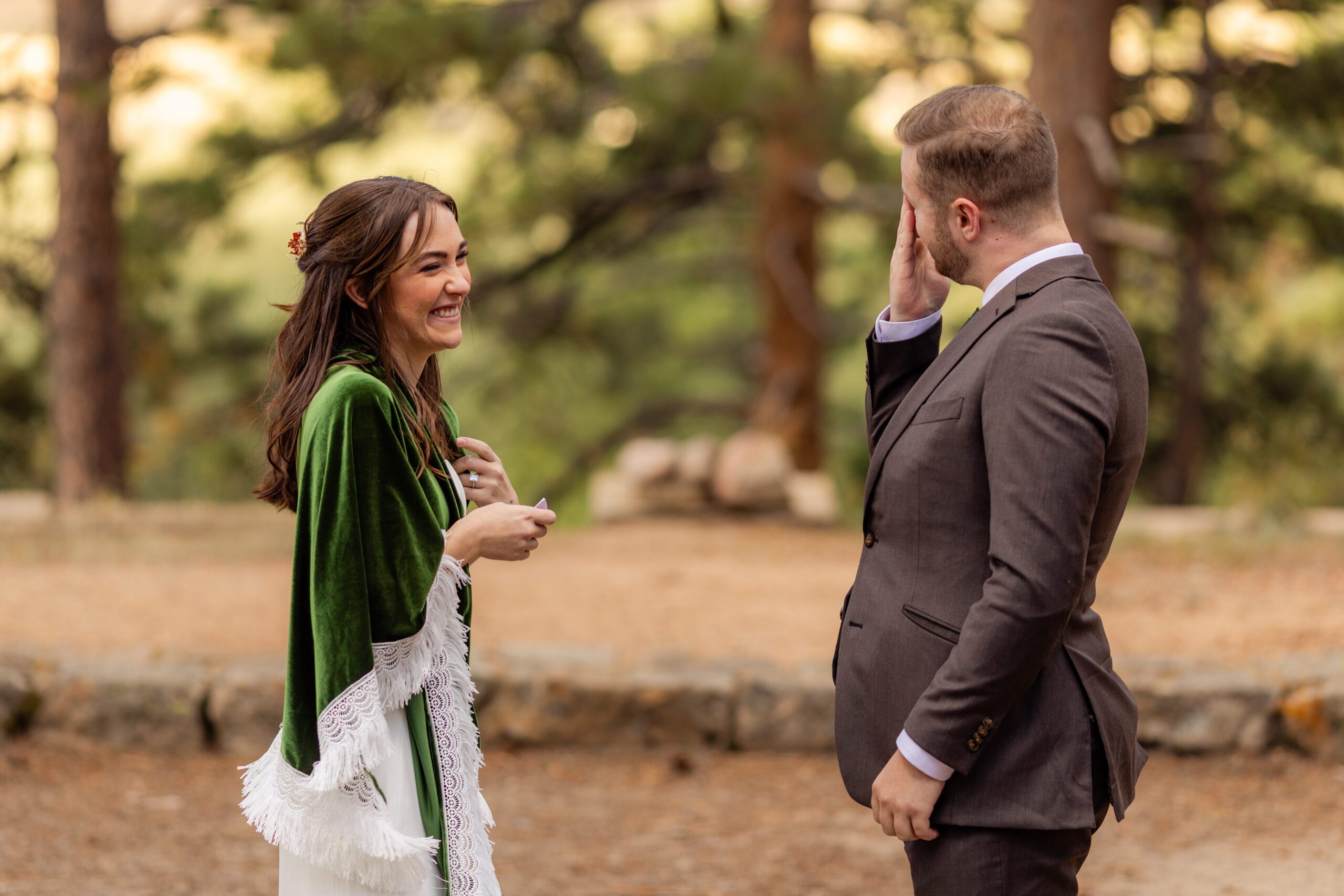 the groom wipes a tear from his eye while his bride smiles at him sweetly during their Dream Lake elopement.