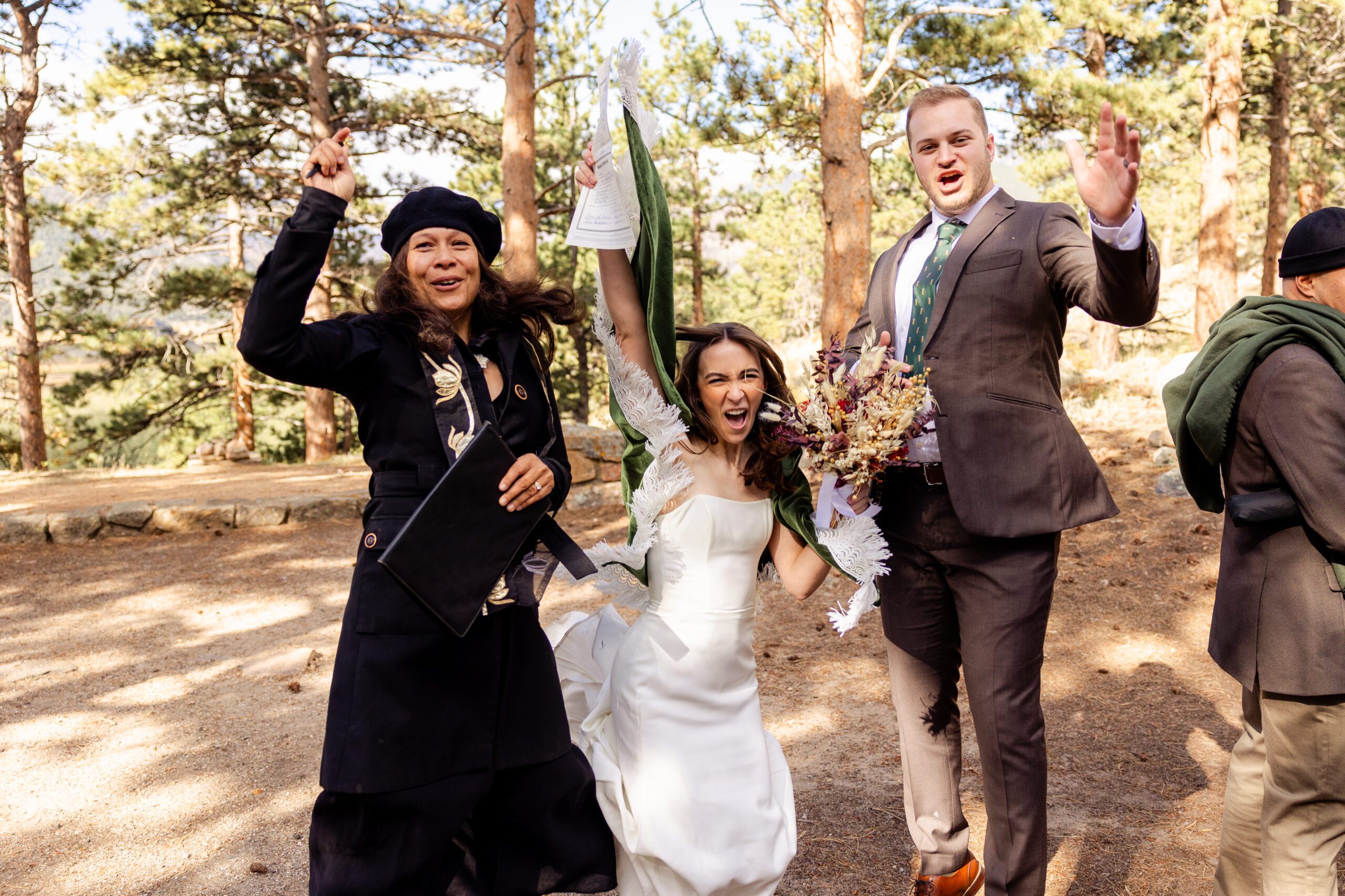 bride and groom raise their hands in celebration with their officiant at their Dream Lake elopement.