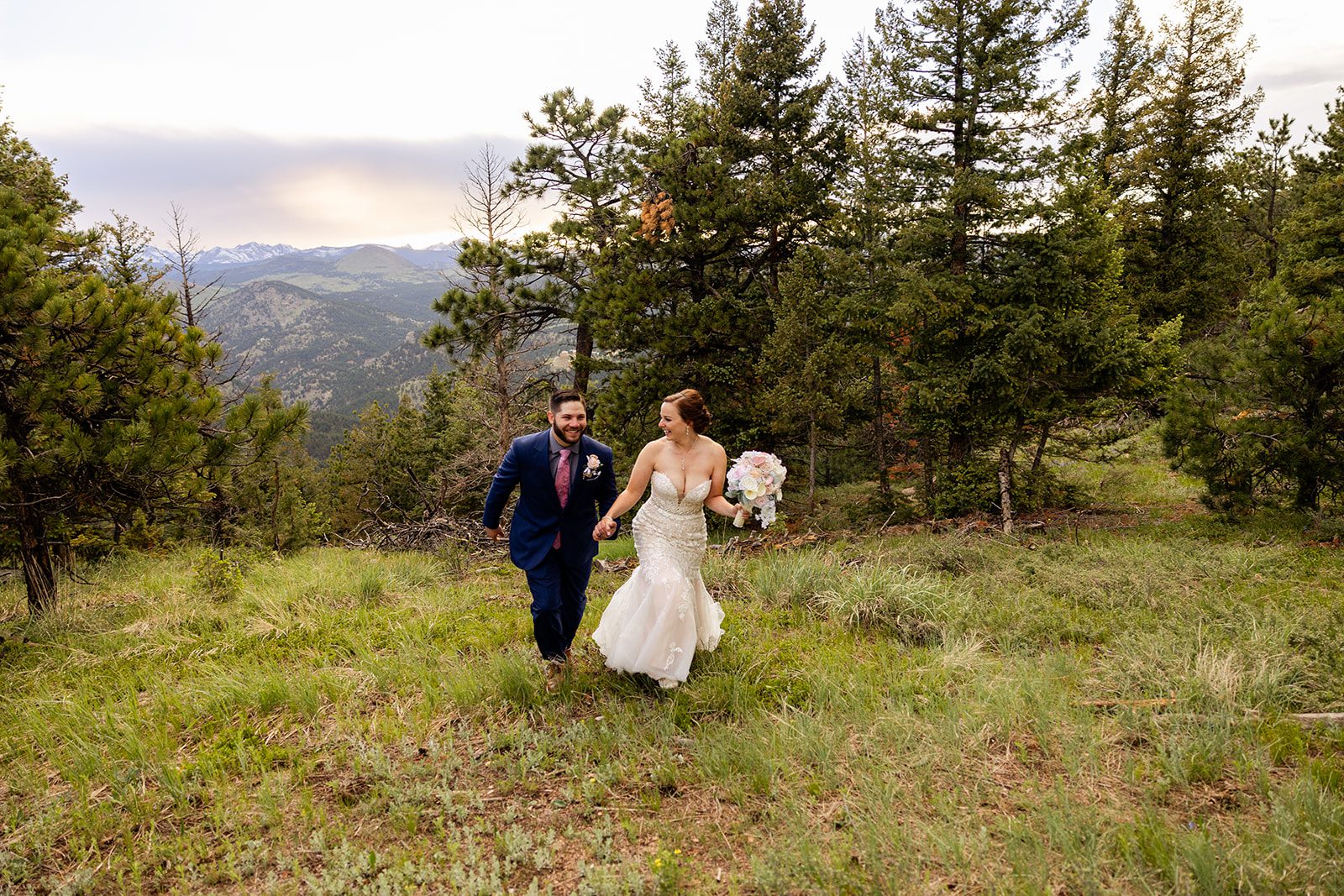bride leads groom by the hand as they frolic through a grassy meadow on their Boulder elopement with videography.