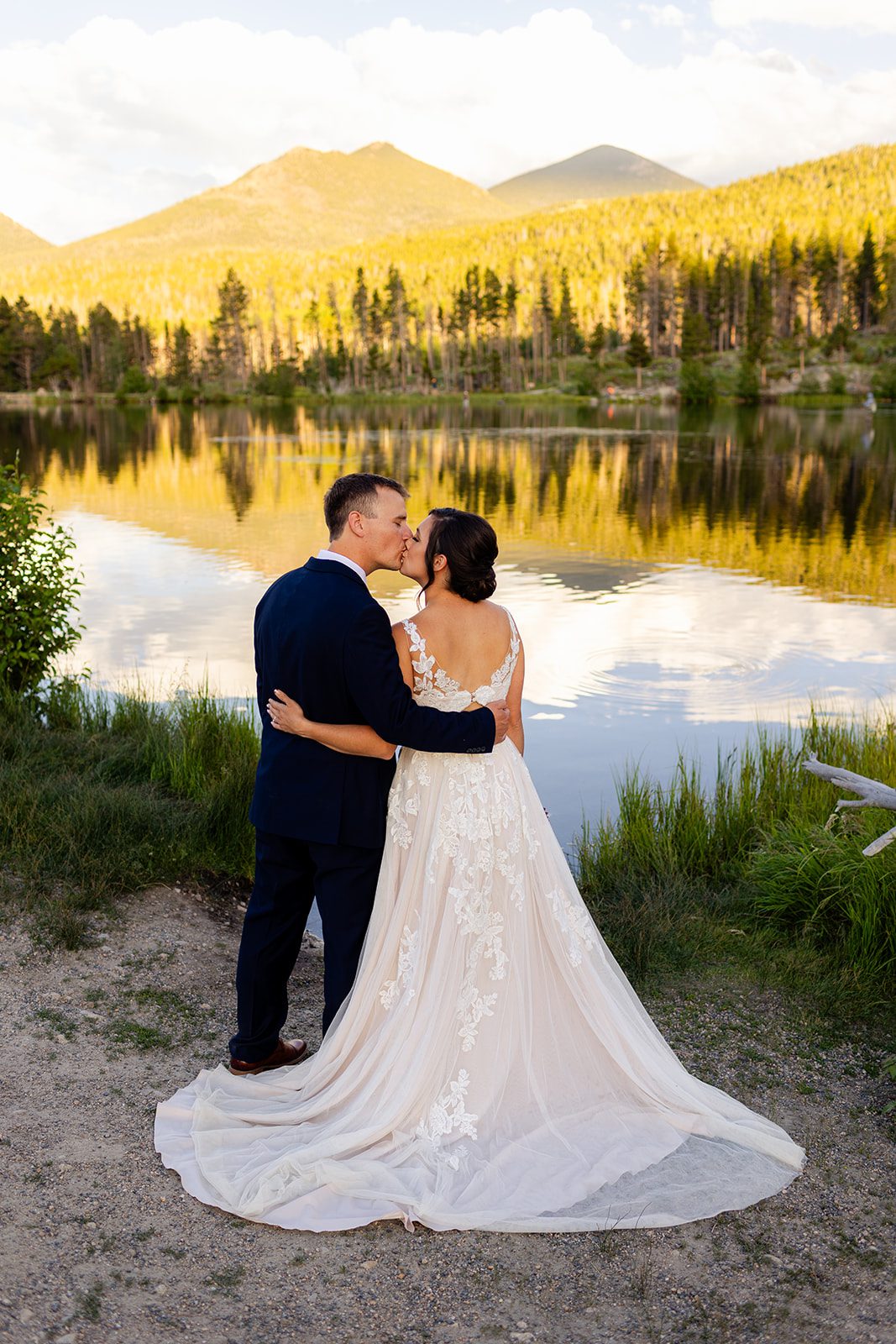 Bride and groom kiss in front of Sprague Lake at sunset for their elopement