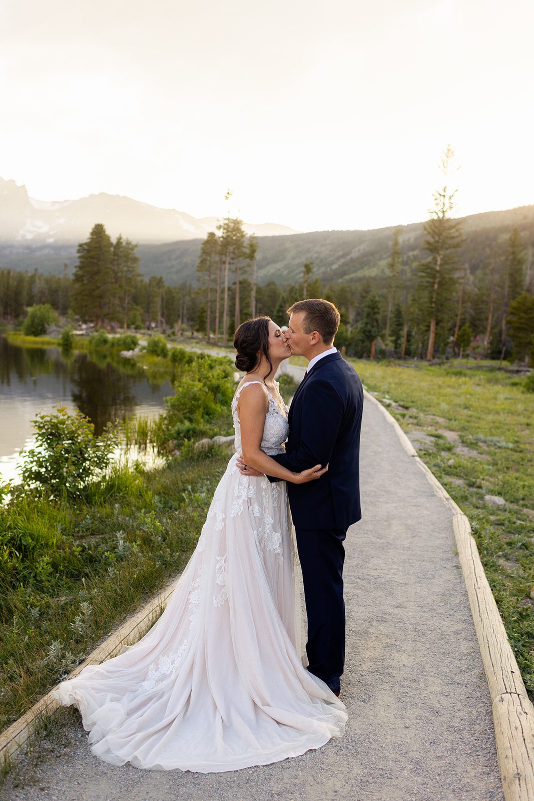 Bride and groom kiss next to Sprague Lake at sunset for their elopement