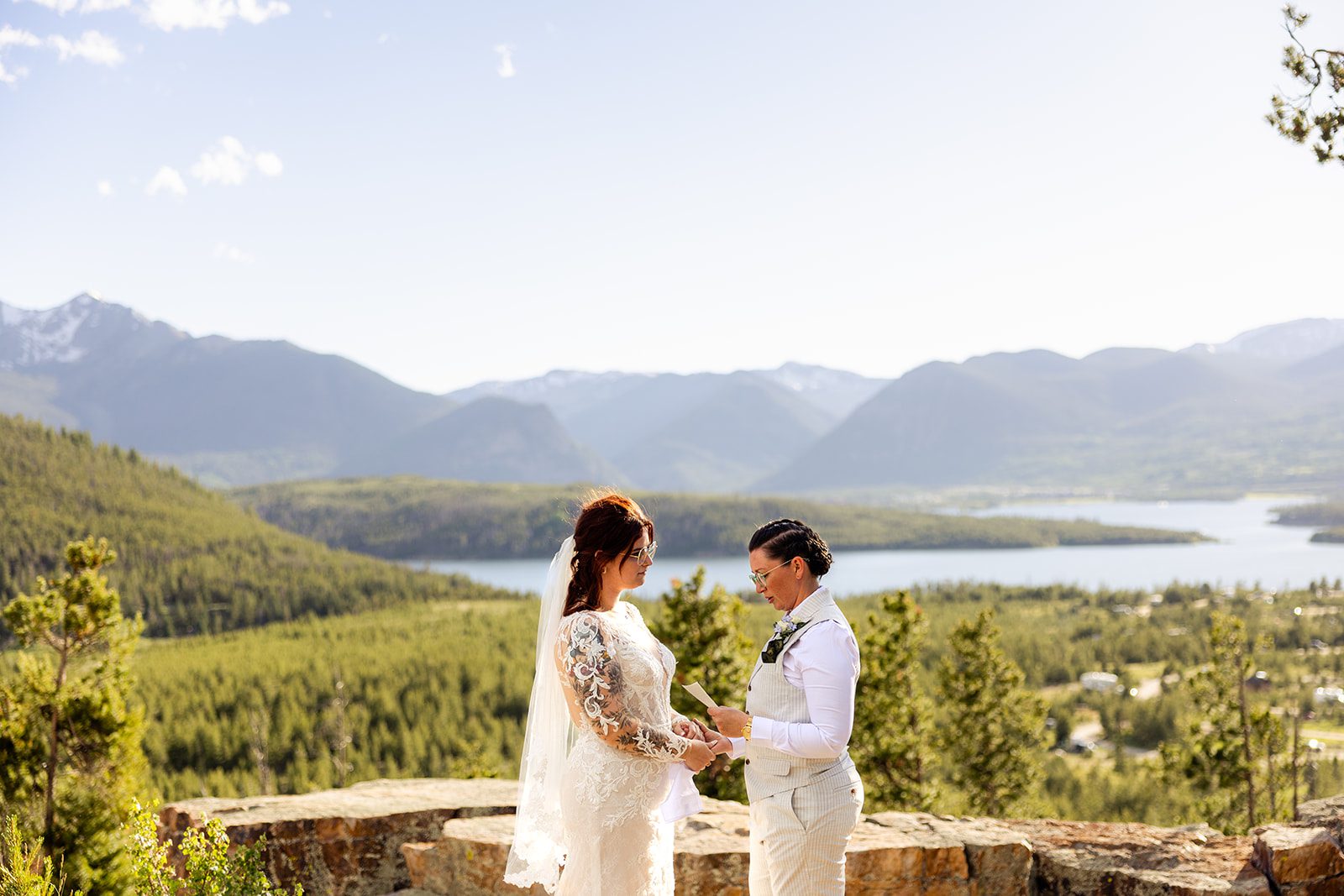 LBGTQ reading vows at sunset, holding hands, pant suit and beautiful Colorado Backdrop during their  Summit County Elopement. 