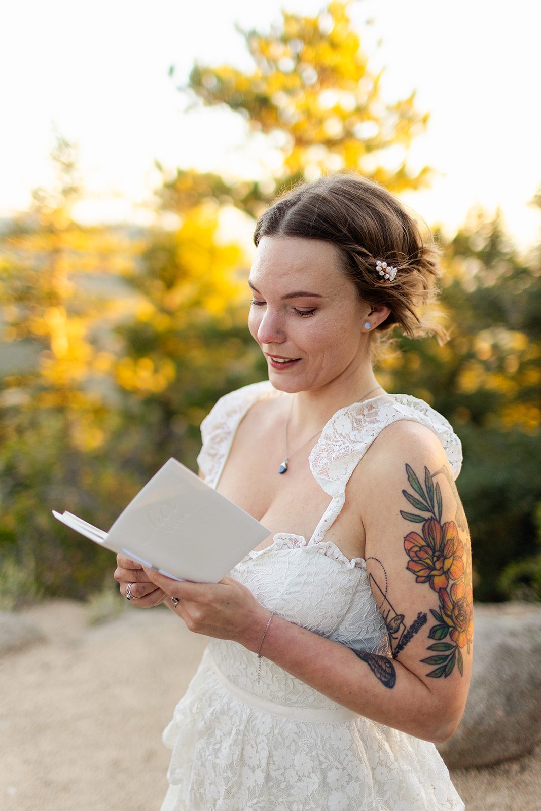 beautiful bride in white gown with tattoos reading her vows during elopement ceremony in Colorado at sunrise at Artist Point.