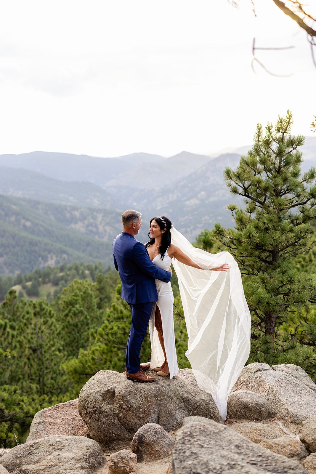 gorgeous bride in a white gown with veil flowing in the wind, with groom after their elopement at artist point. 